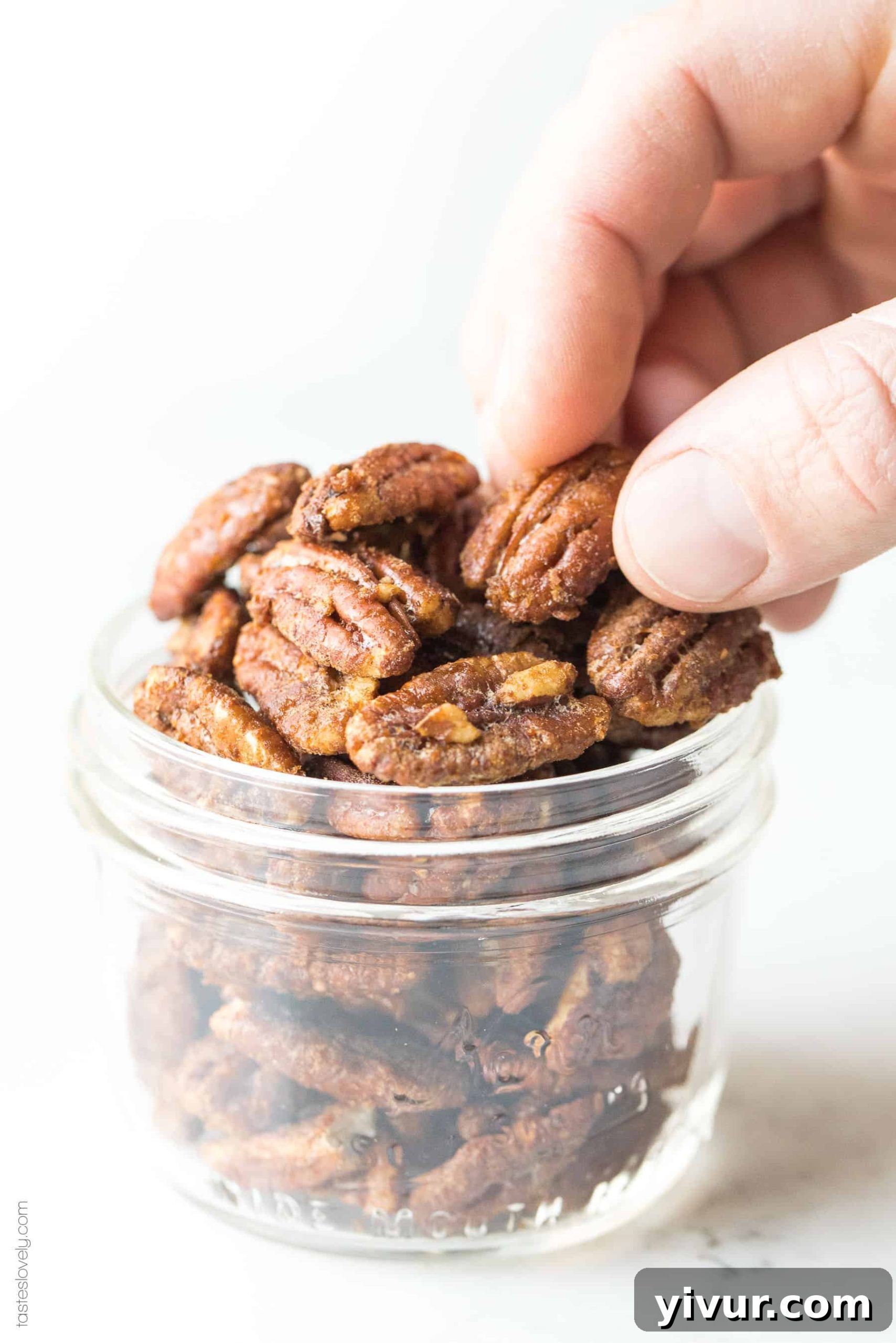 Hand picking up a perfectly glazed paleo candied pecan, showcasing its sweet and crunchy texture.