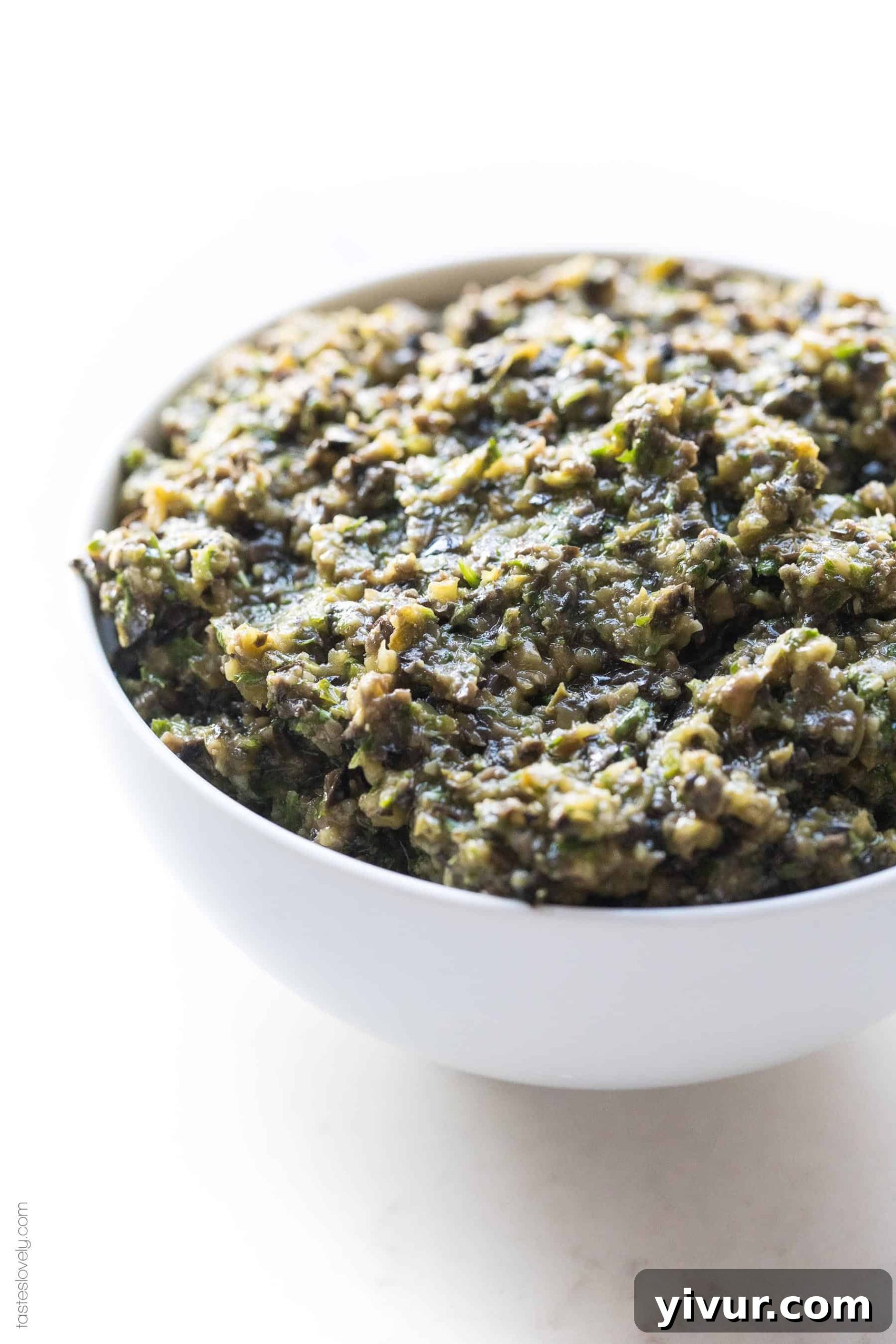 A white bowl filled with olive tapenade, garnished with fresh parsley, ready to be served.