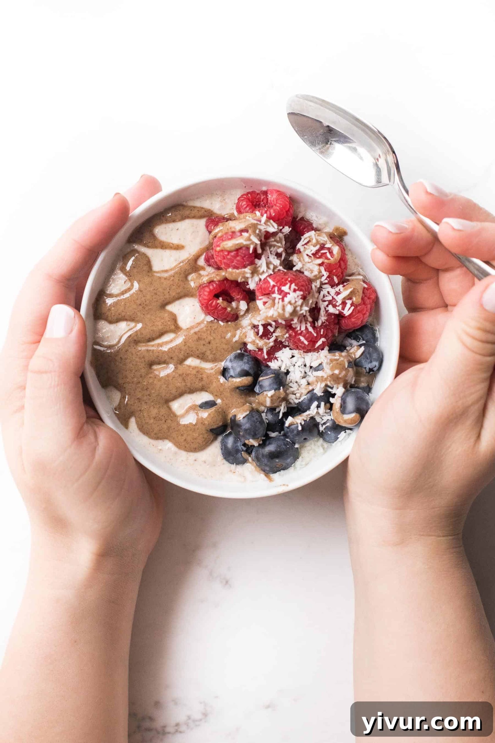 Two hands gently holding a bowl of warm almond pulp breakfast porridge, garnished with vibrant berries and creamy nut butter, an ideal paleo and whole30 breakfast.