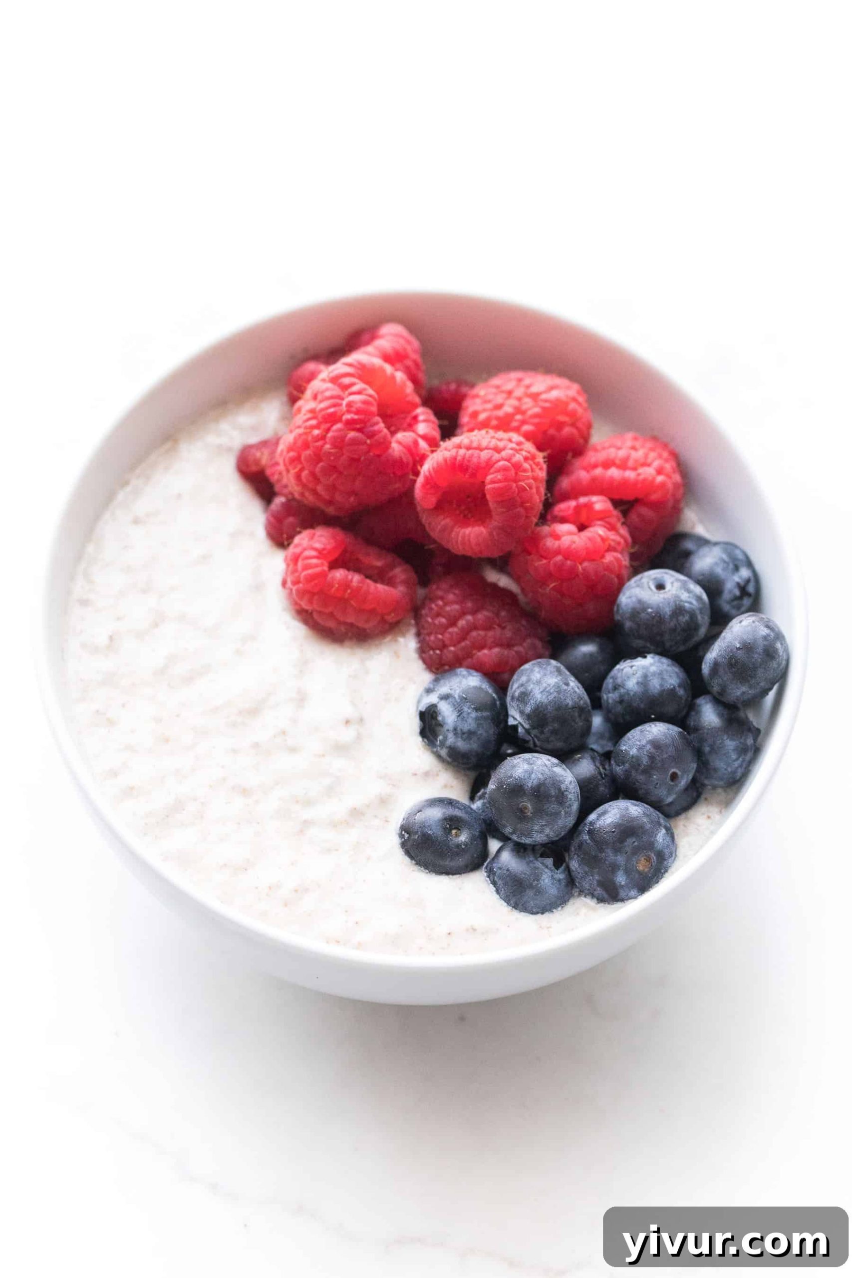 A crisp white bowl filled with creamy almond pulp breakfast porridge, garnished with a medley of fresh raspberries and blueberries, perfect for a paleo and whole30 diet.