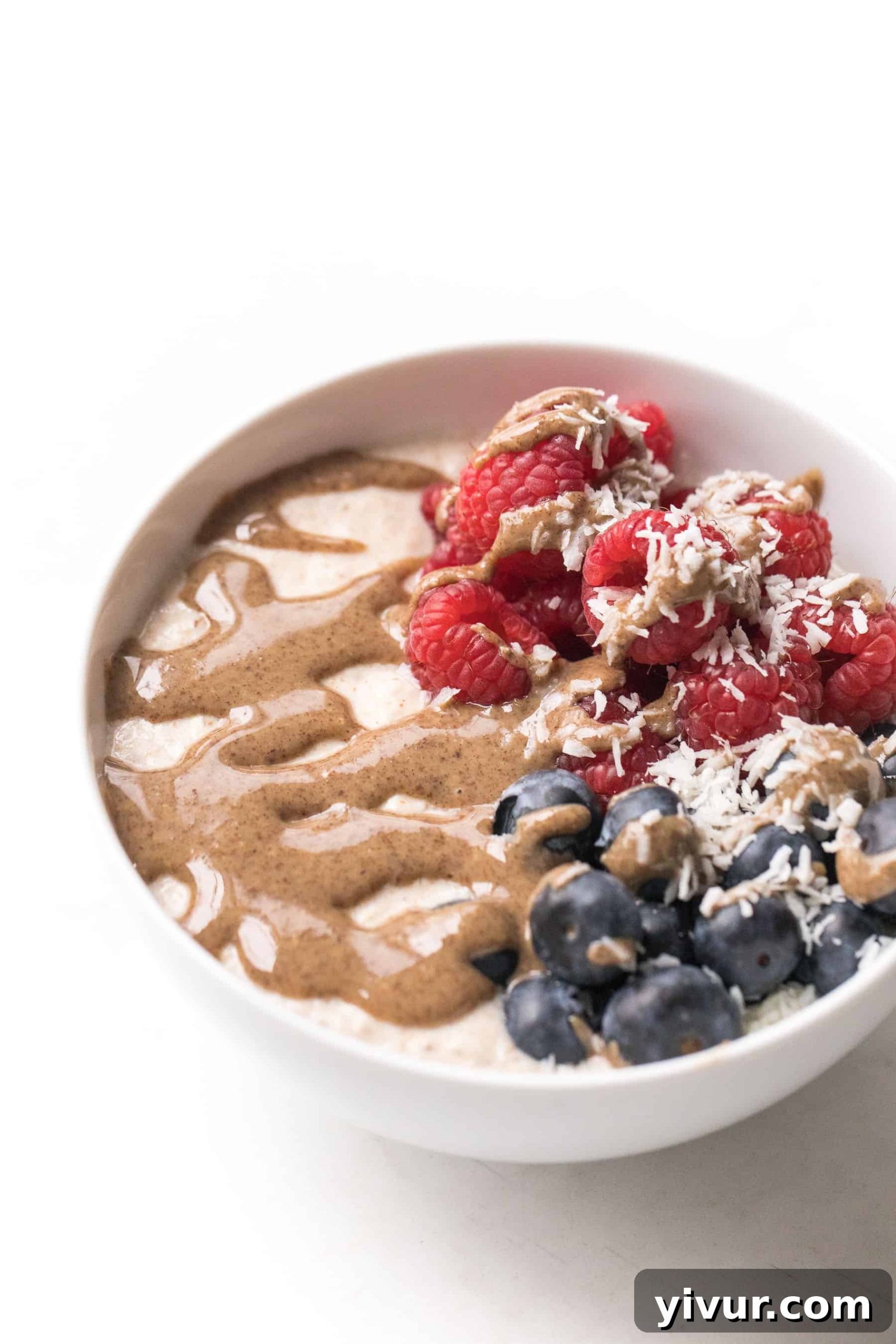 A beautifully presented white bowl of almond pulp breakfast porridge, topped with fresh berries and a swirl of creamy nut butter, highlighting its appeal as a paleo and whole30 breakfast.