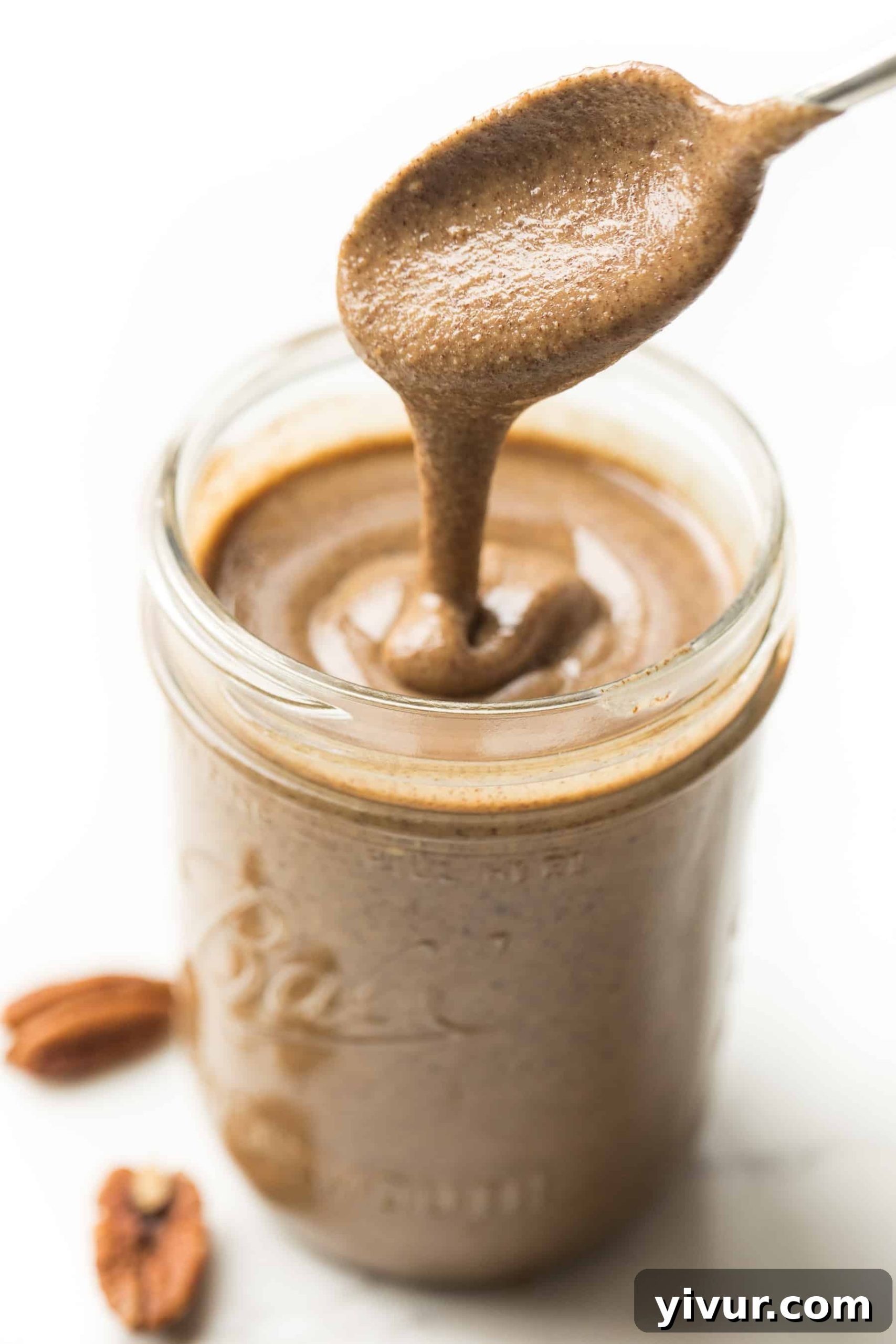 Creamy Paleo Whole30 Homemade Pecan Butter 2 Creamy homemade pecan butter being drizzled from a spoon into a clear mason jar, showcasing its smooth texture for a Paleo and Whole30 diet.