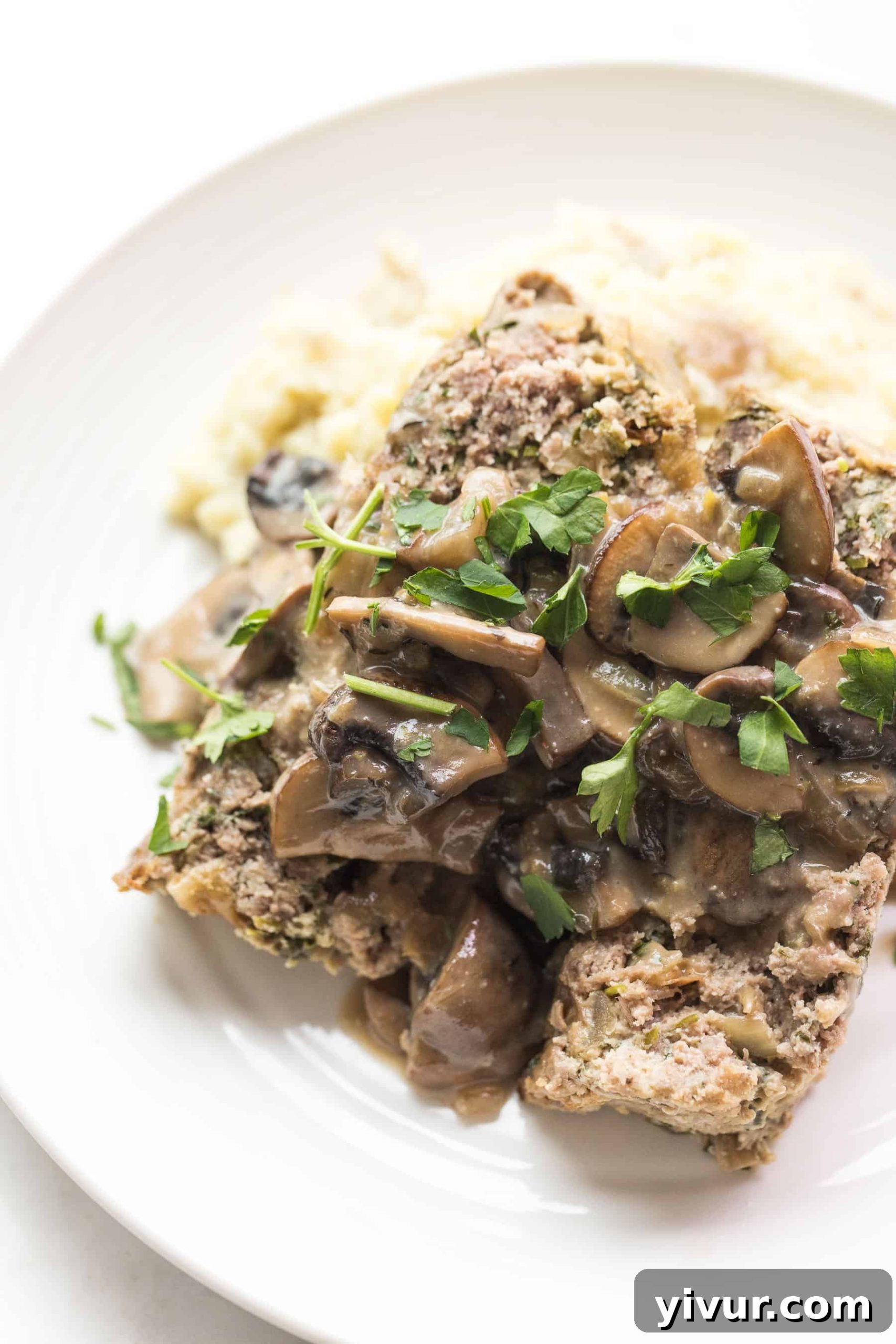 White plate with meatloaf and mushroom gravy over mashed potatoes