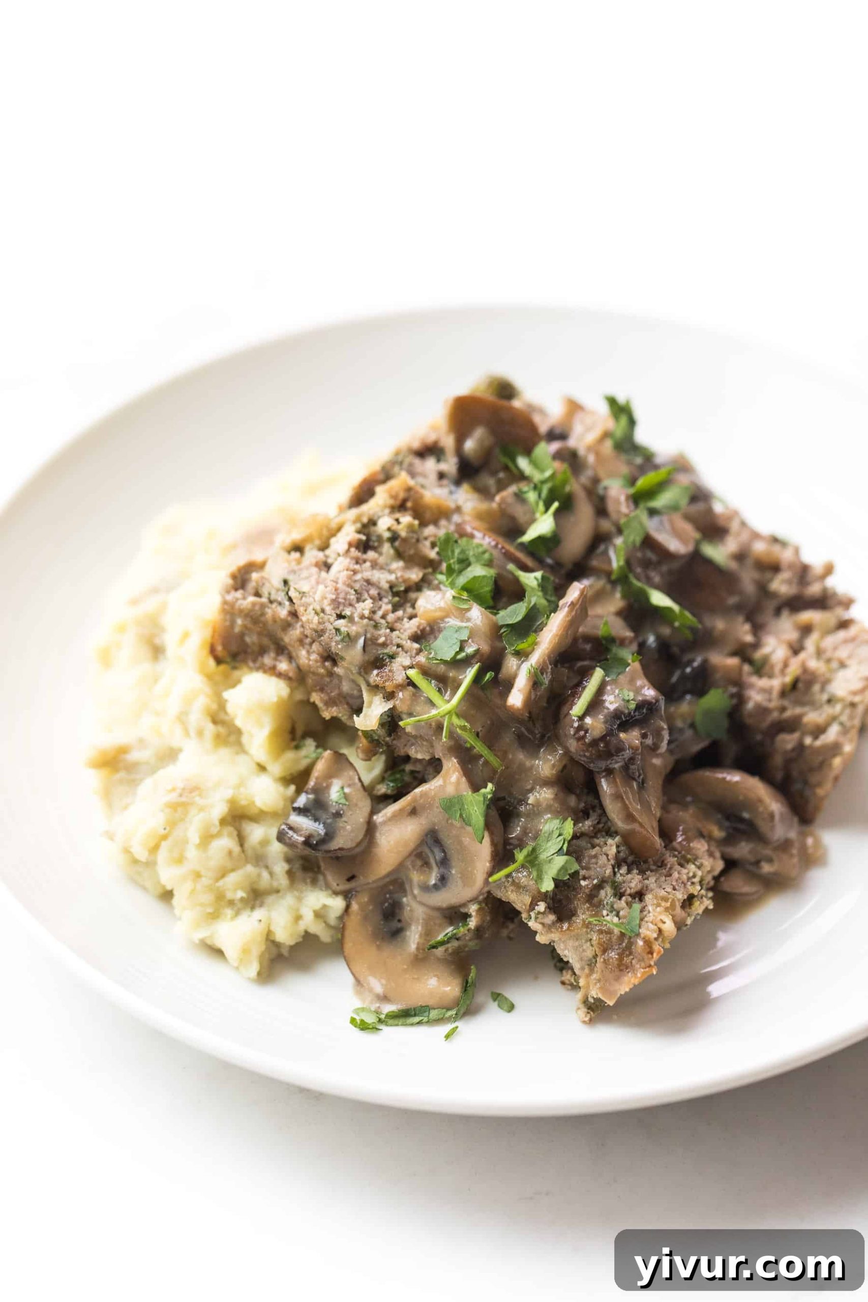 White plate with meatloaf and mushroom gravy over mashed potatoes
