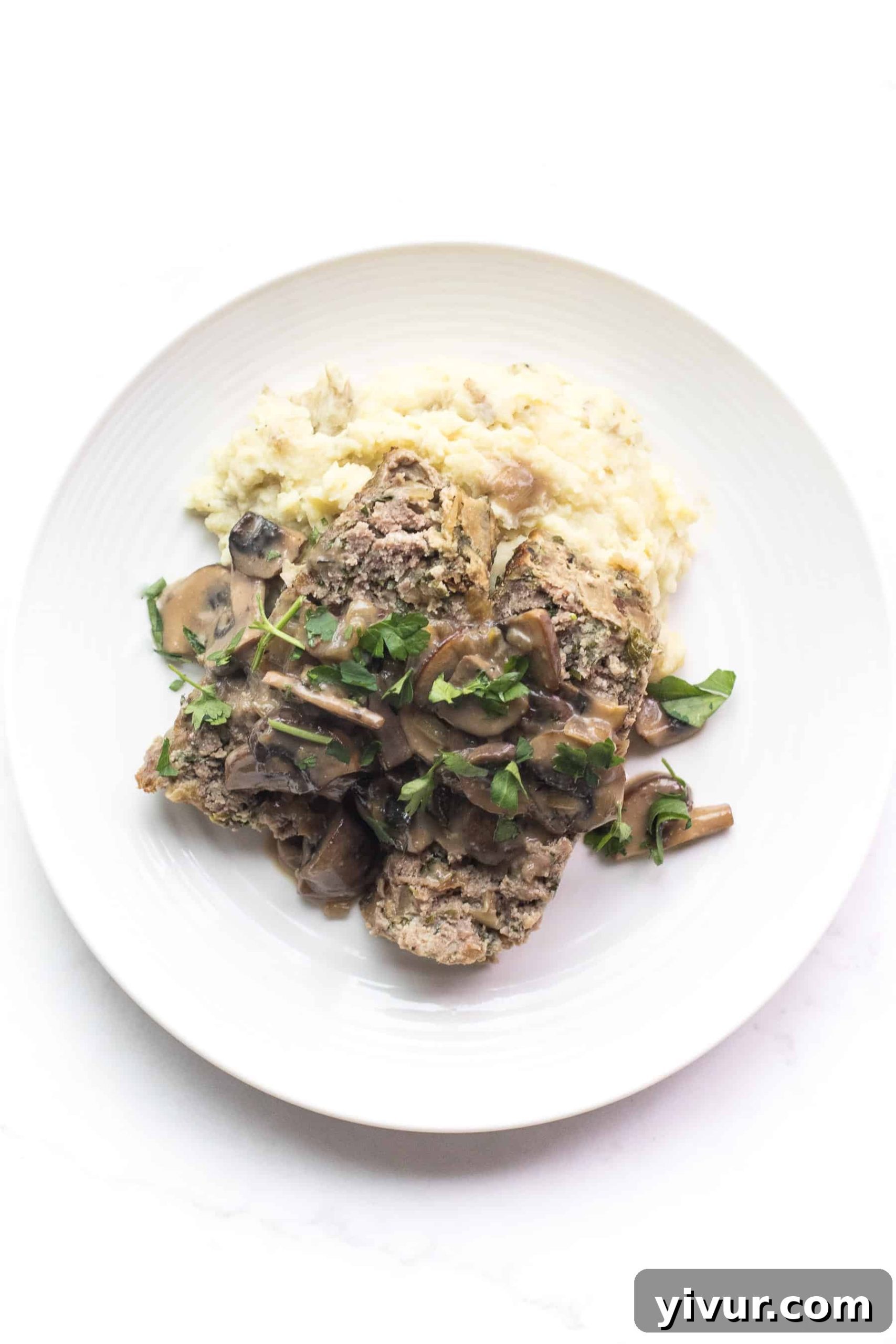 white plate with meatloaf and mushroom gravy over mashed potatoes
