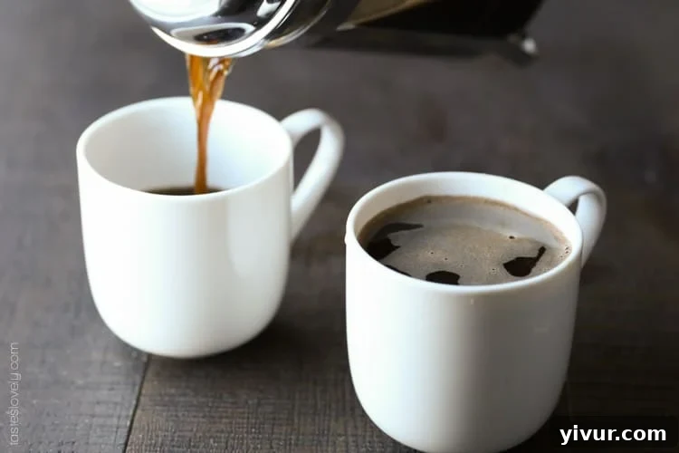 Unlock Barista-Quality French Press Coffee At Home 3 Two white coffee mugs on a dark surface being filled with the best french press recipe.