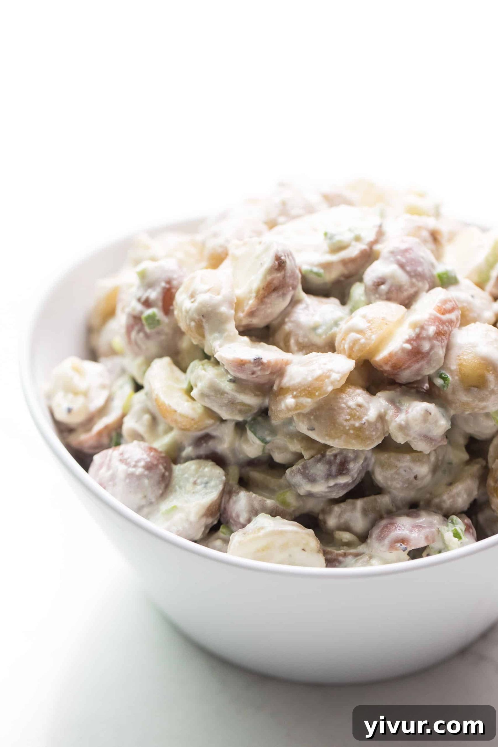 Close-up of a bowl of creamy potato salad on a pristine white background