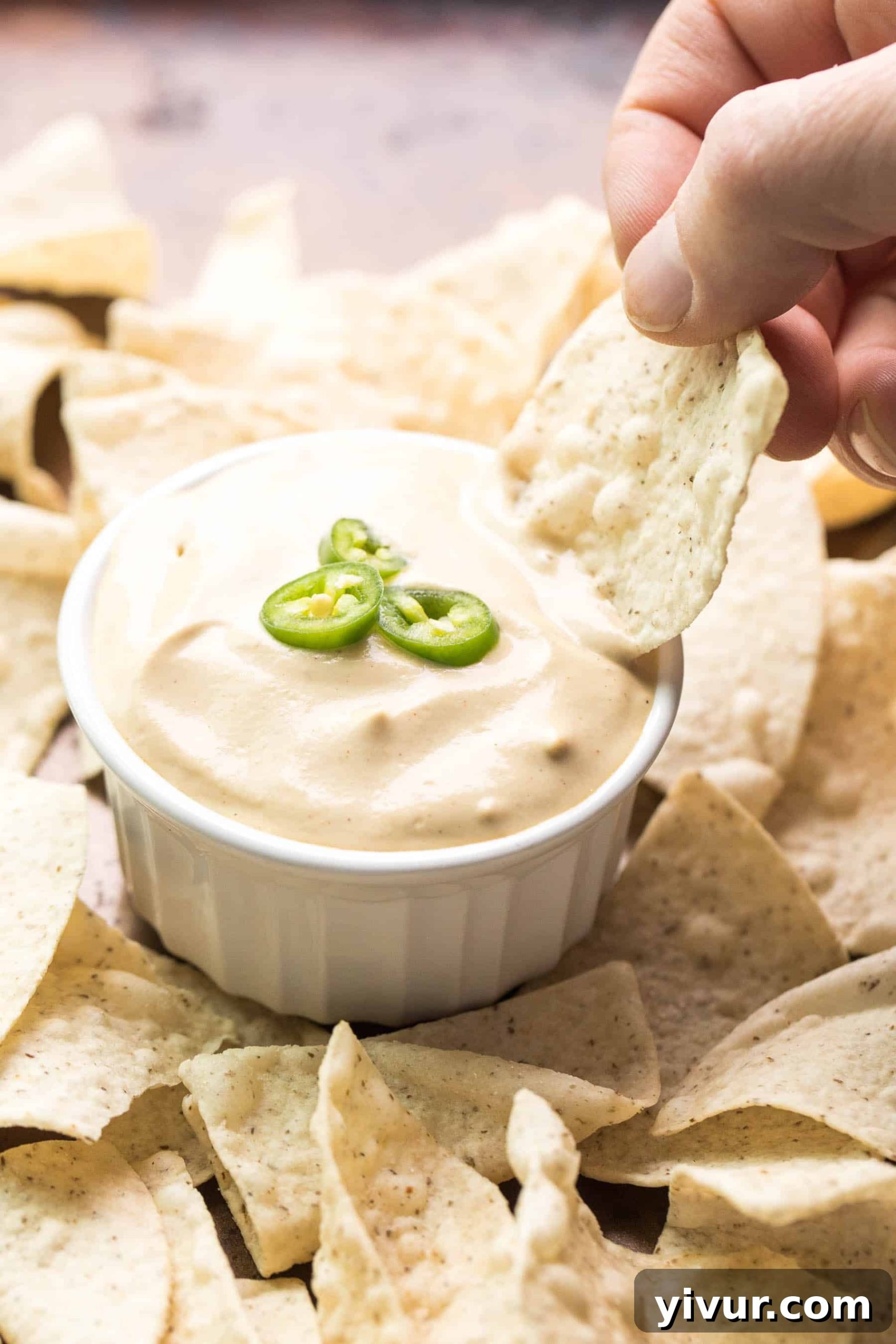 A close-up shot of a hand dipping a crispy tortilla chip into a bowl of creamy, delicious queso nacho cheese, ready for enjoyment.