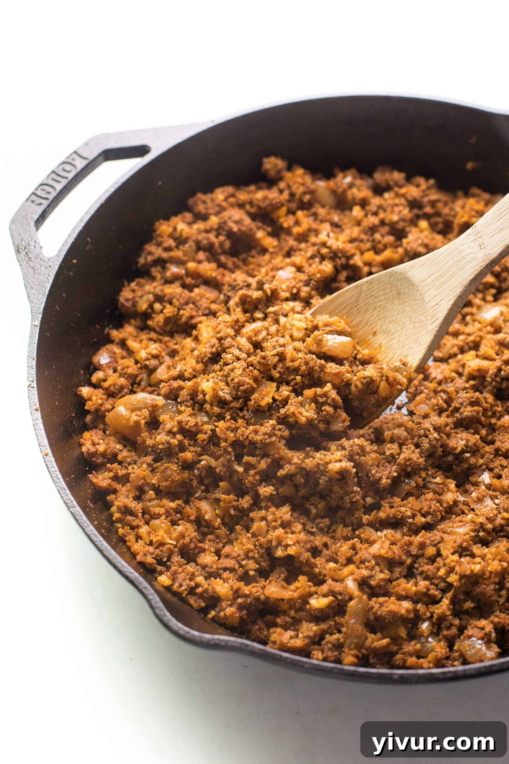 Ground beef taco meat cooked with cauliflower rice and taco seasoning in a cast iron skillet with a spoon, ready to serve.