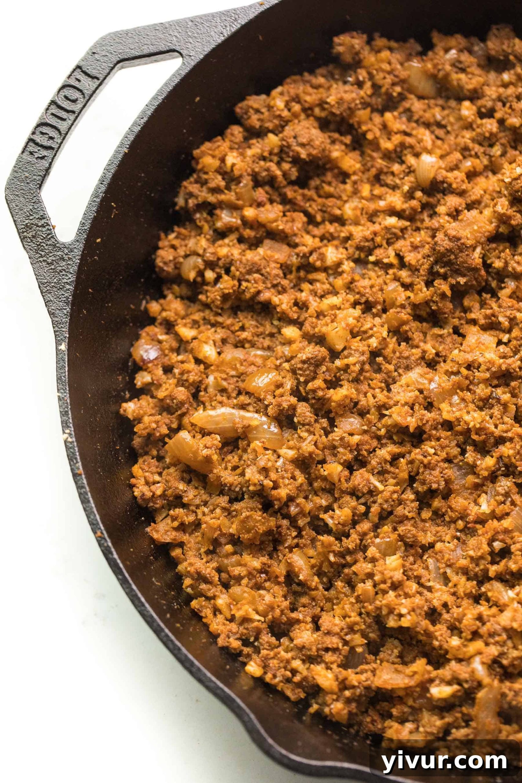 Top-down view of cooked ground beef taco meat in a cast iron skillet on a white background, garnished with cilantro.