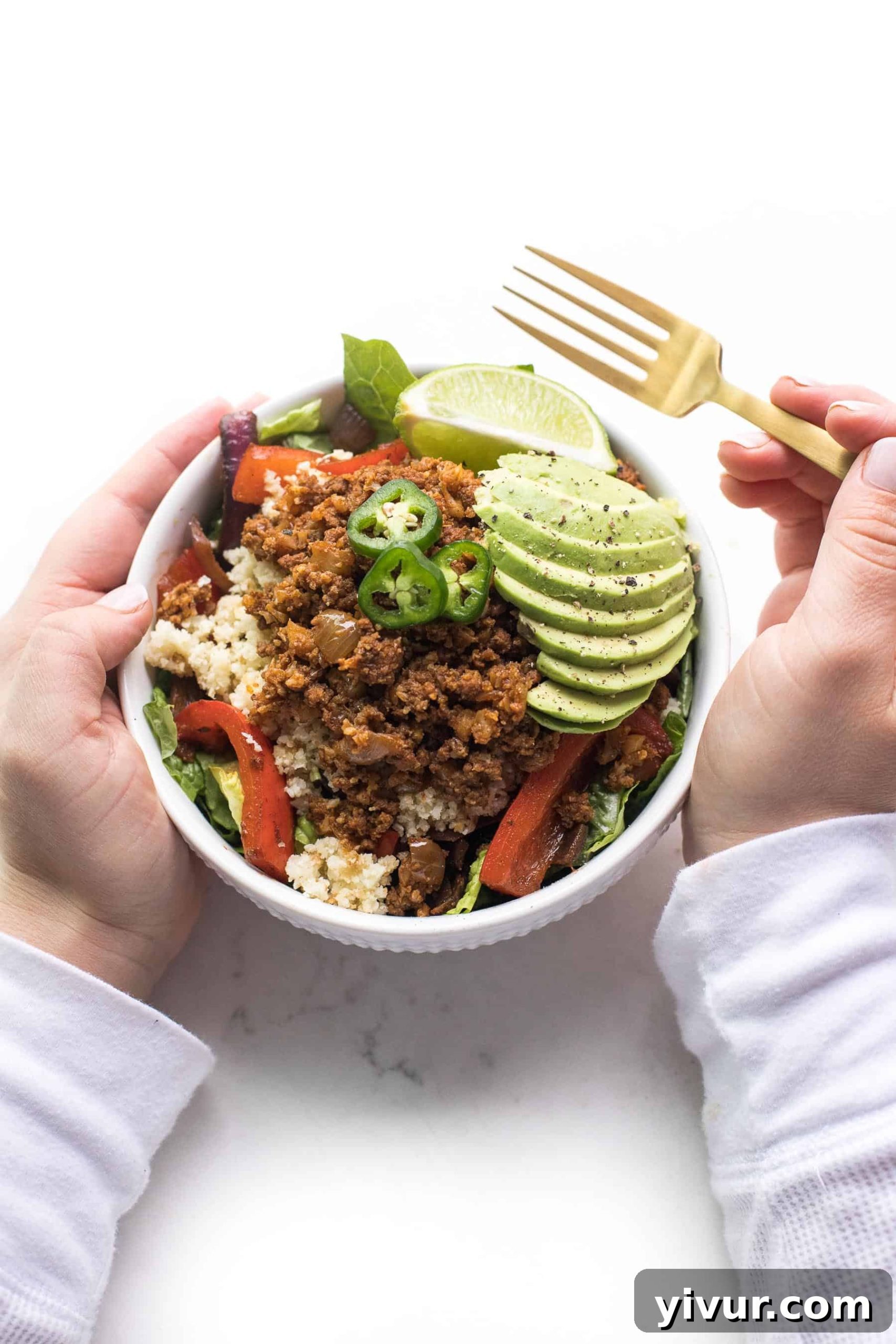 2 hands holding a burrito bowl with a gold fork in the right hand
