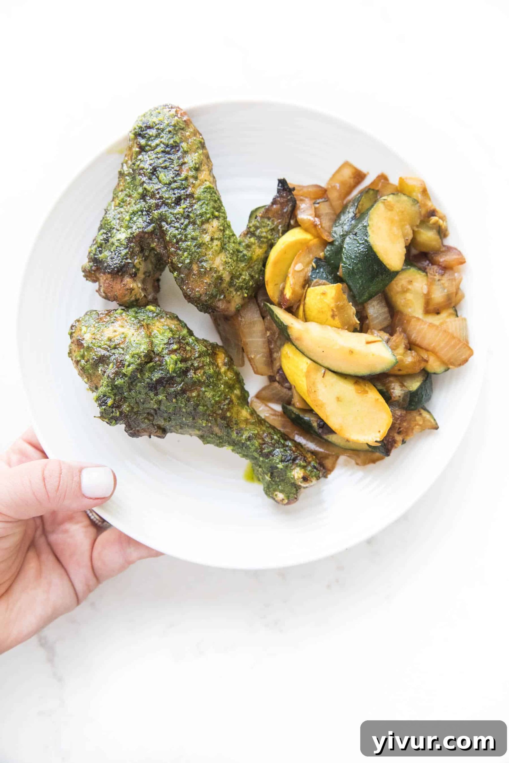 Zesty Grilled Chimichurri Chicken: Whole30, Keto & Paleo 3 A white plate showcasing succulent grilled chicken, richly adorned with fresh chimichurri sauce, accompanied by perfectly cooked squash on a pristine white background.