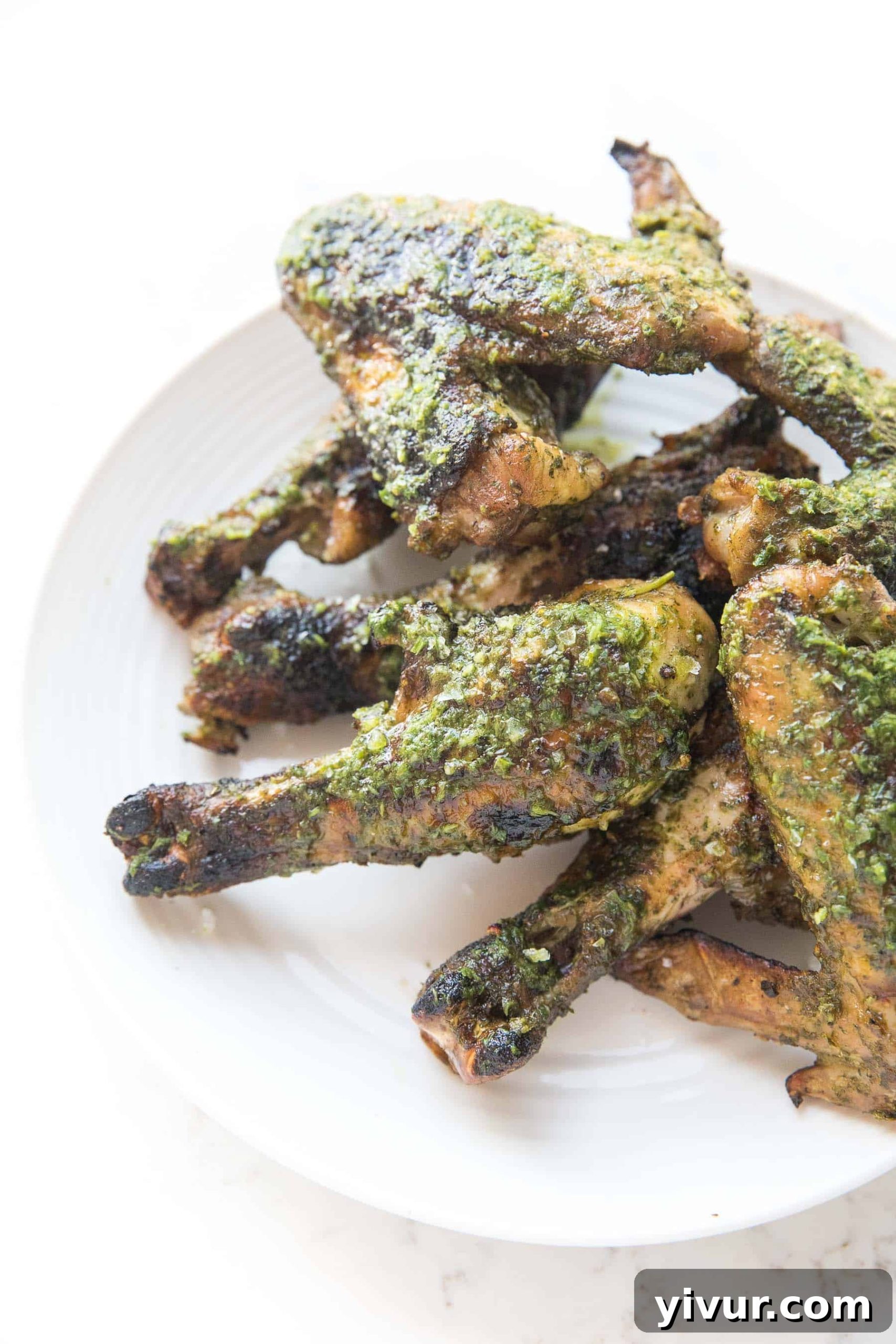 Zesty Grilled Chimichurri Chicken: Whole30, Keto & Paleo 5 Artfully arranged grilled chicken drumsticks and wings, each glistening with fresh chimichurri sauce, presented on a pristine white plate and background.