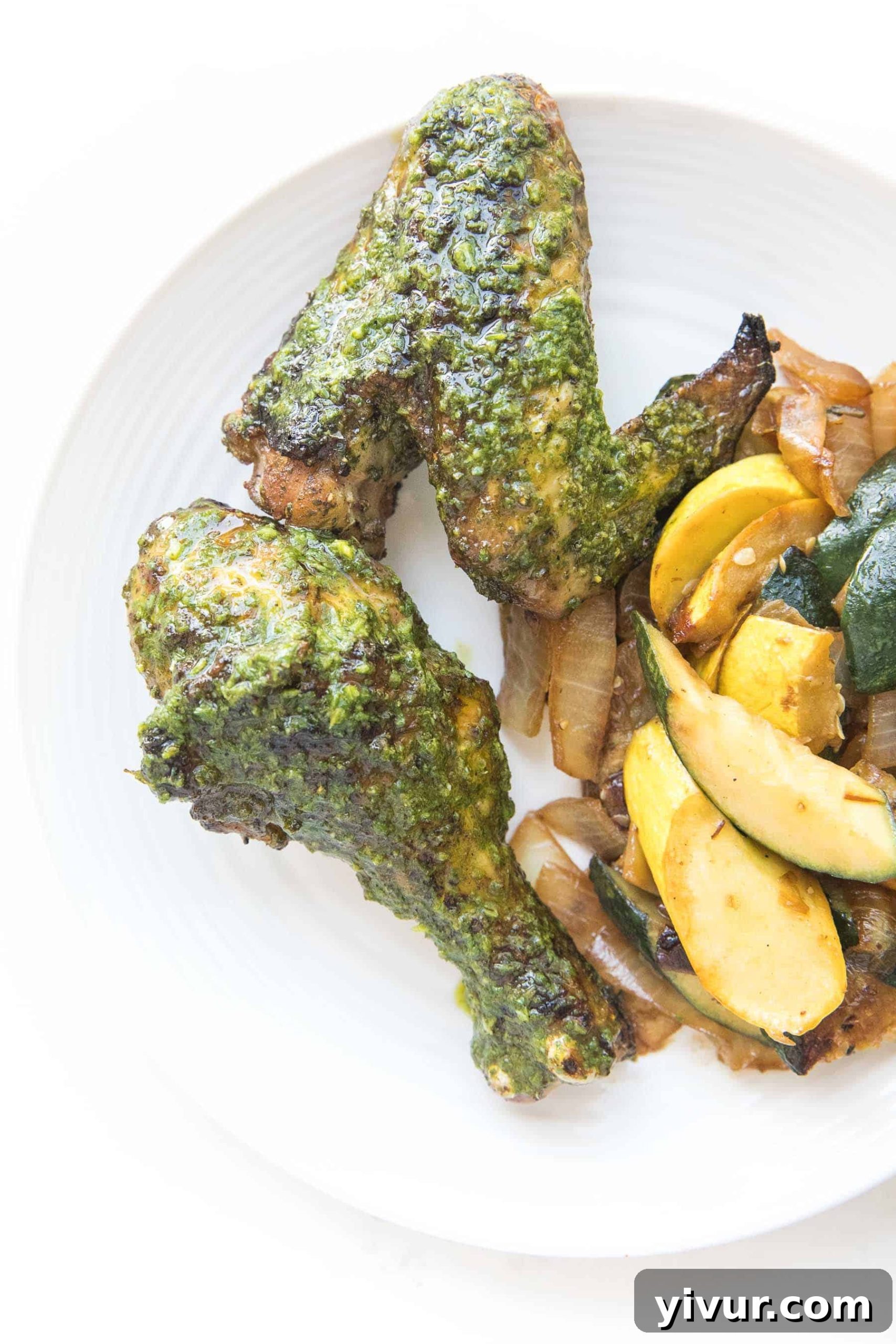 Zesty Grilled Chimichurri Chicken: Whole30, Keto & Paleo 6 A white plate filled with savory grilled chicken drumsticks and wings, accompanied by tender roasted squash, all arranged beautifully on a pristine white background.