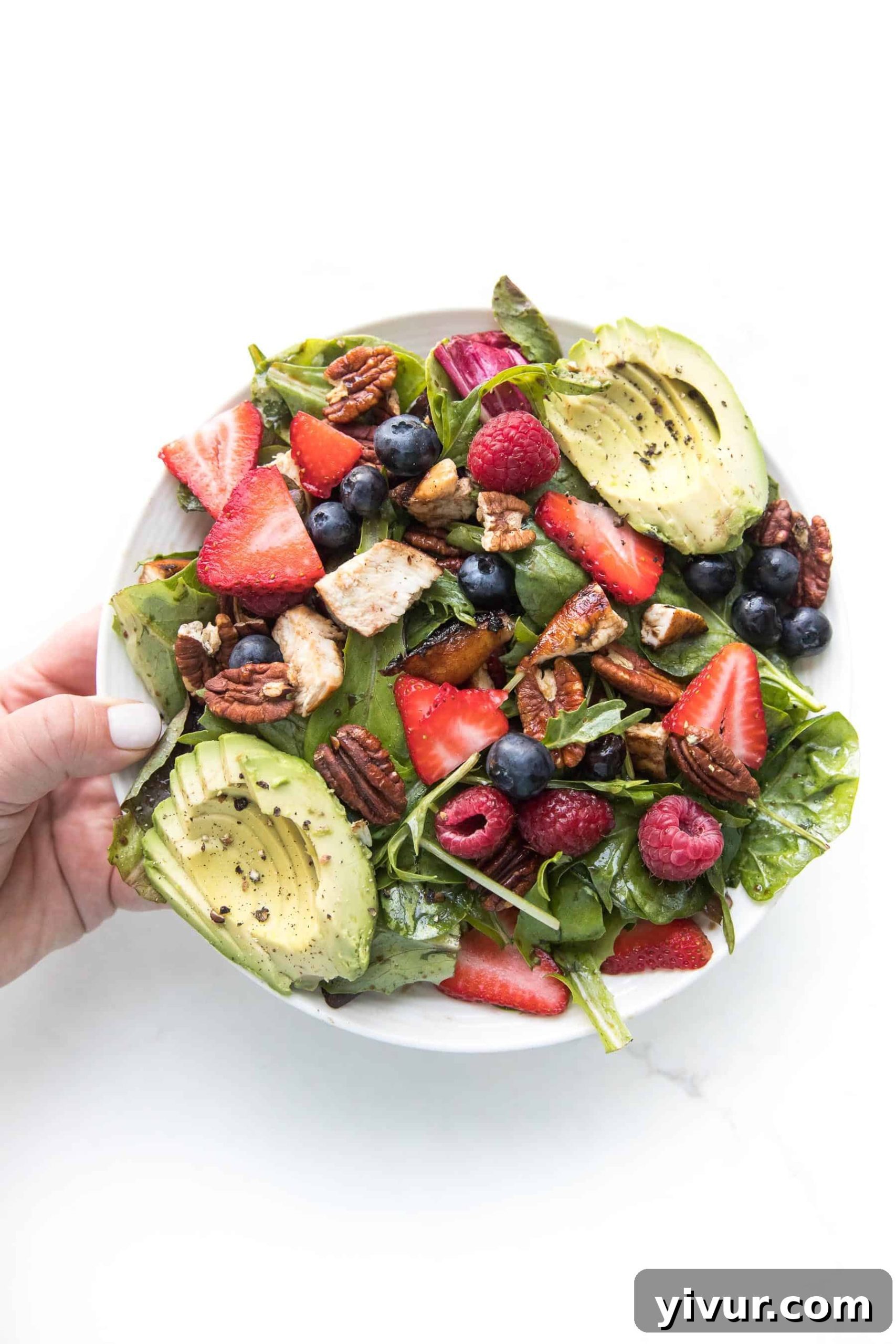 Vibrant Whole30 Keto Balsamic Chicken Berry Salad 3 A close-up shot of a hand holding a forkful of Whole30 + Keto Balsamic Chicken Berry Salad, highlighting the fresh ingredients and inviting texture.