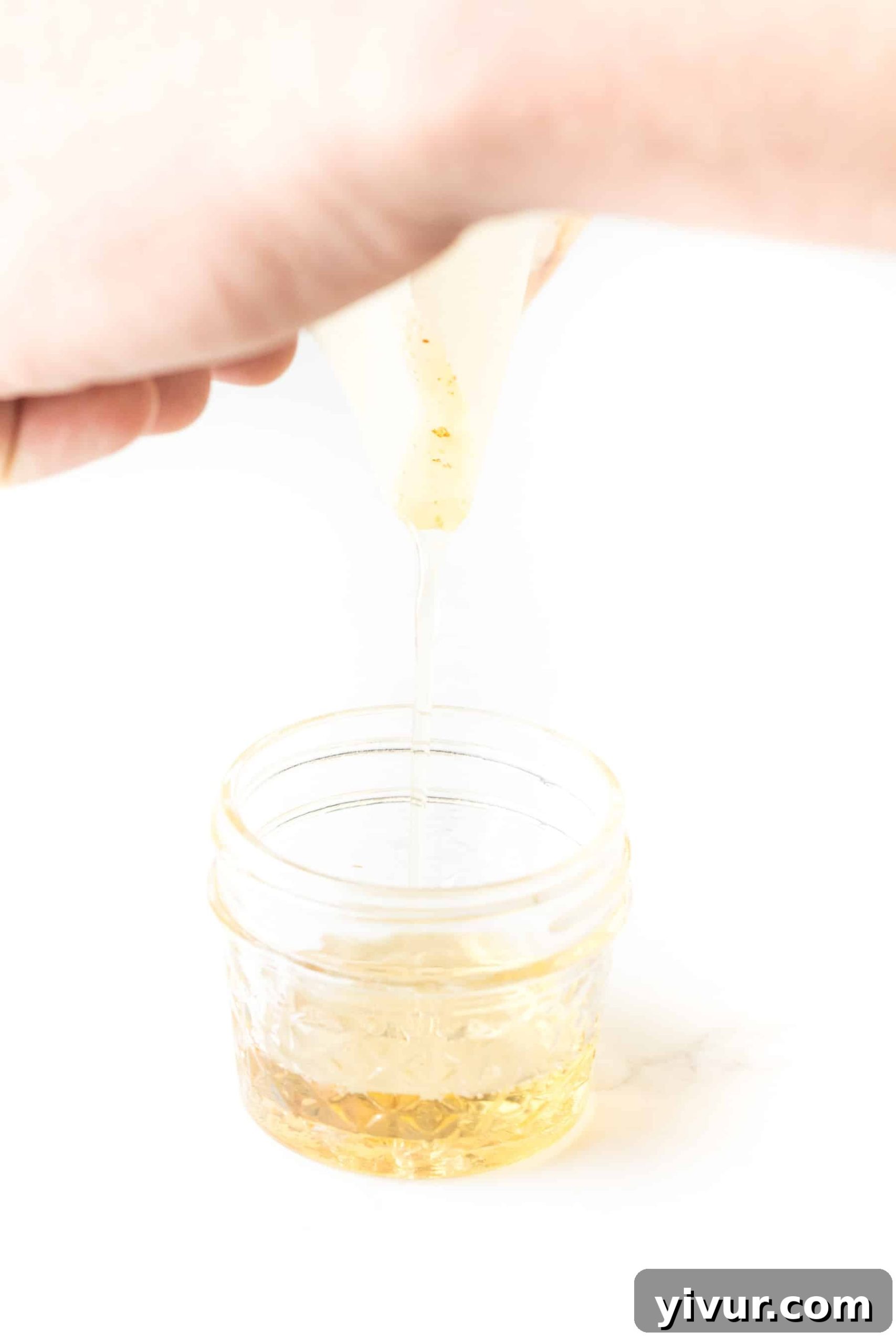 A hand carefully pouring hot bacon grease from a baking sheet into a clear mason jar, illustrating the process of saving bacon drippings for future use.