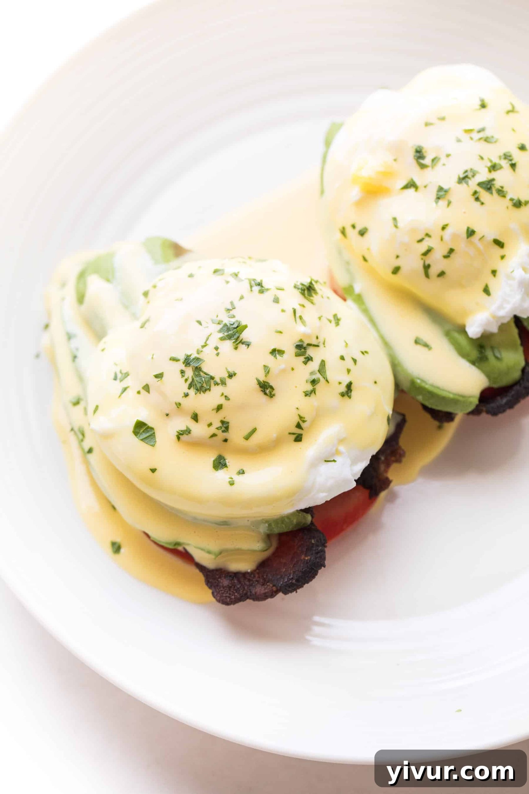 Close-up of keto eggs benedict garnished with green herbs on a white plate.