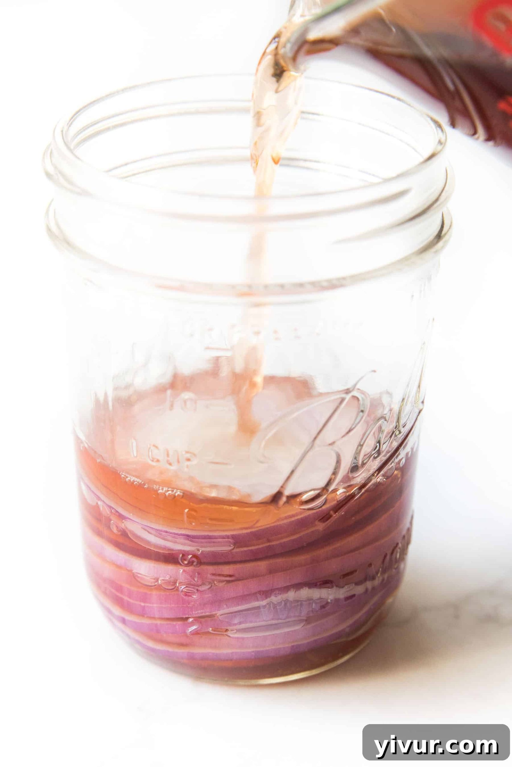 pouring red wine vinegar over pickled onions on a white background