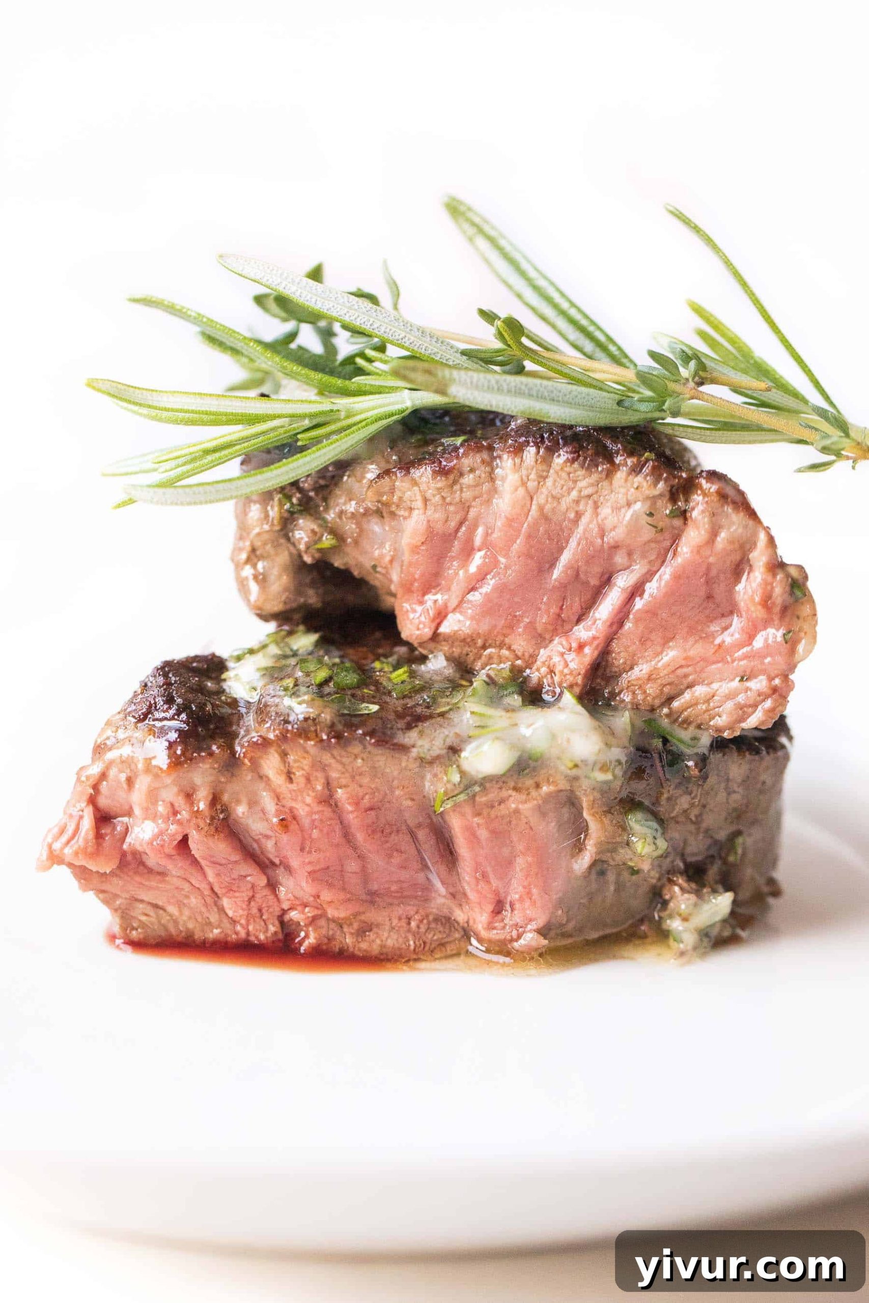 Perfectly seared filet mignon topped with a generous dollop of dairy-free herb butter, presented on a pristine white plate against a minimalist white background.
