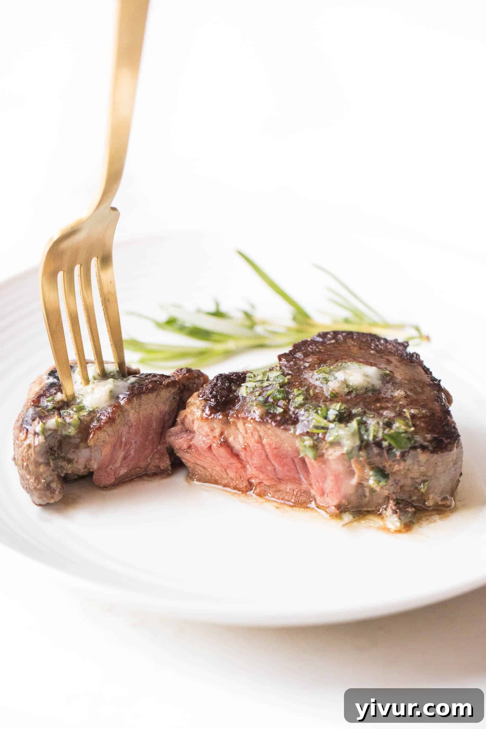 A close-up view of a perfectly cooked filet mignon, sliced in half to reveal its tender, juicy medium-rare center, topped with a melting dairy-free herb butter, presented on a white plate.