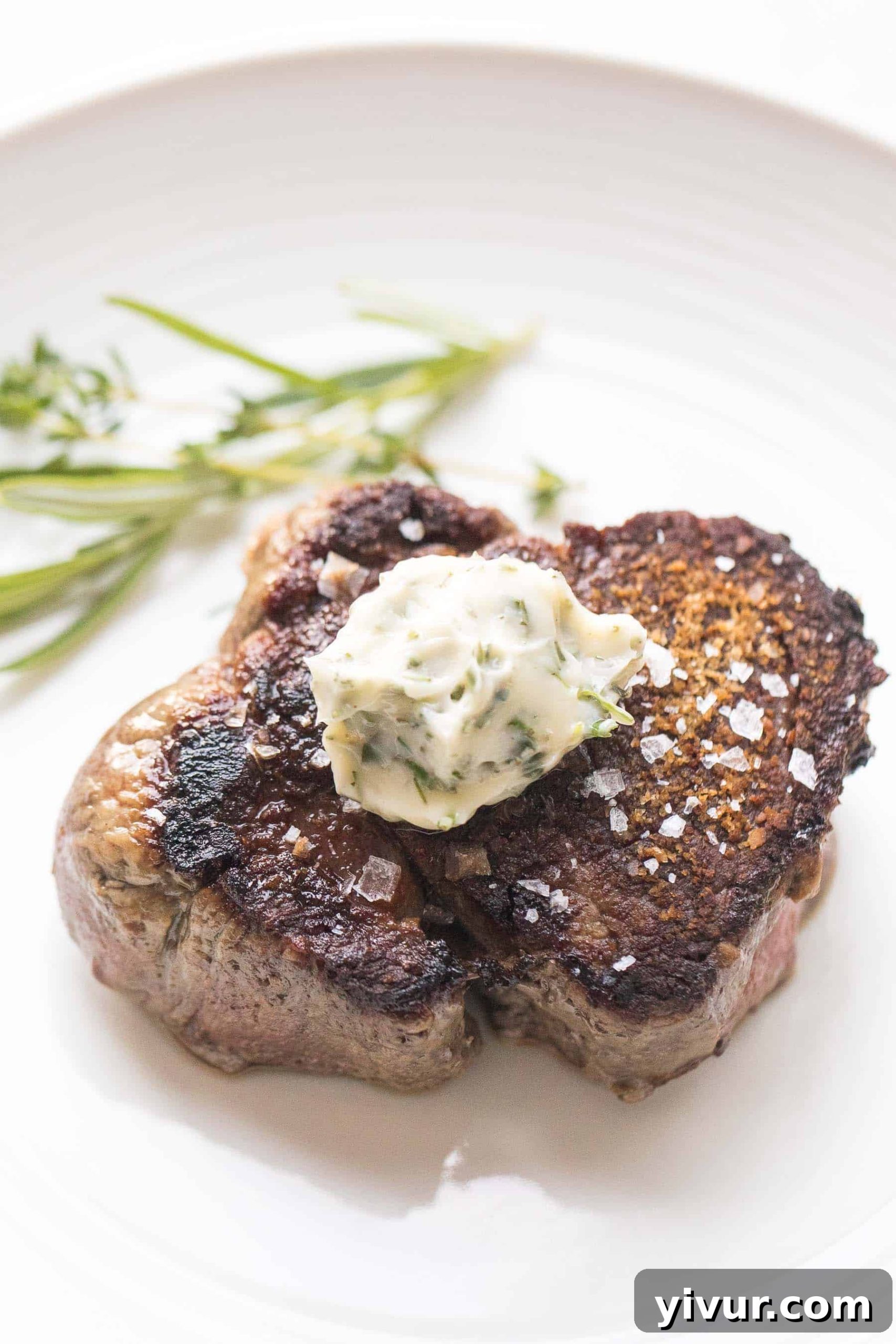 Another enticing image of perfectly cooked filet mignon, adorned with melting herb butter, served on a clean white plate against a light background.