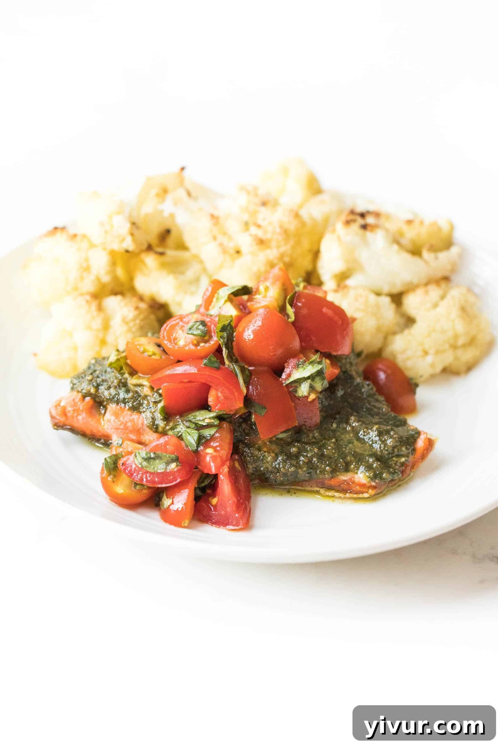 Caprese Pesto Salmon for Whole30 and Keto 2 Crispy skin salmon topped with vibrant pesto and fresh Caprese marinated tomatoes on a white plate