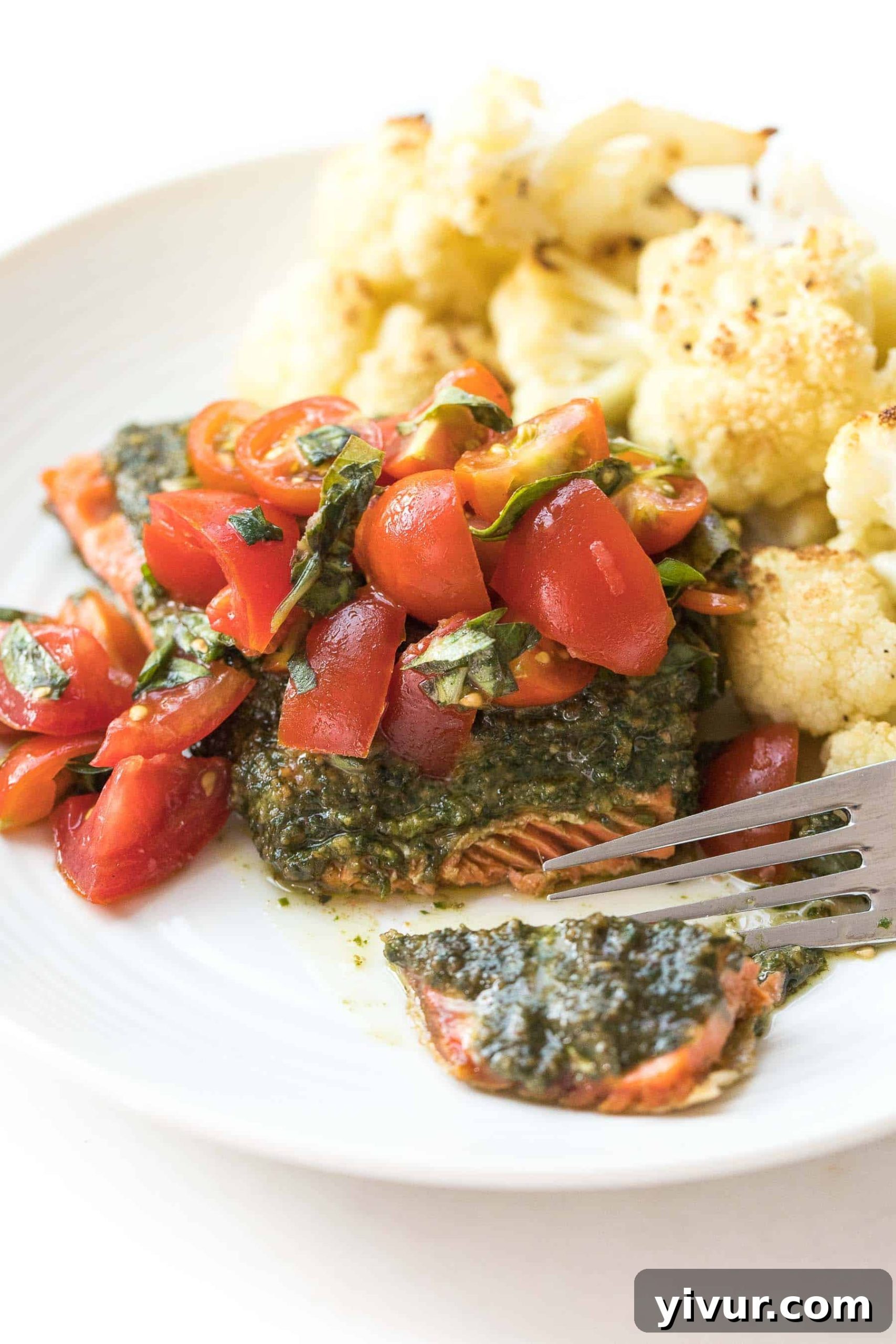 Caprese Pesto Salmon for Whole30 and Keto 3 A fork cutting into a perfectly cooked salmon filet with crispy skin, pesto, and Caprese tomatoes