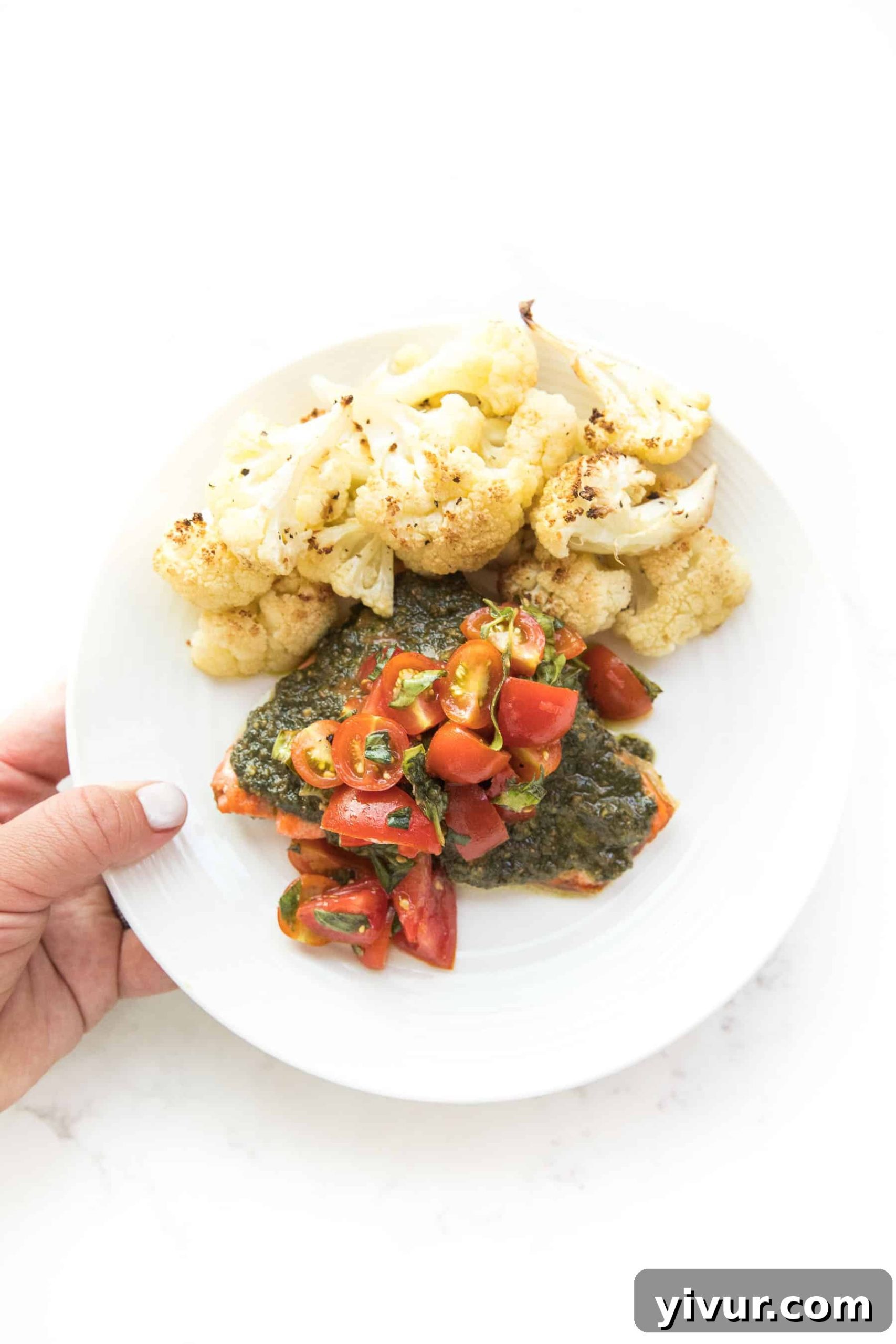 Caprese Pesto Salmon for Whole30 and Keto 5 A hand holding a white plate with Caprese Pesto Salmon, showcasing the inviting presentation