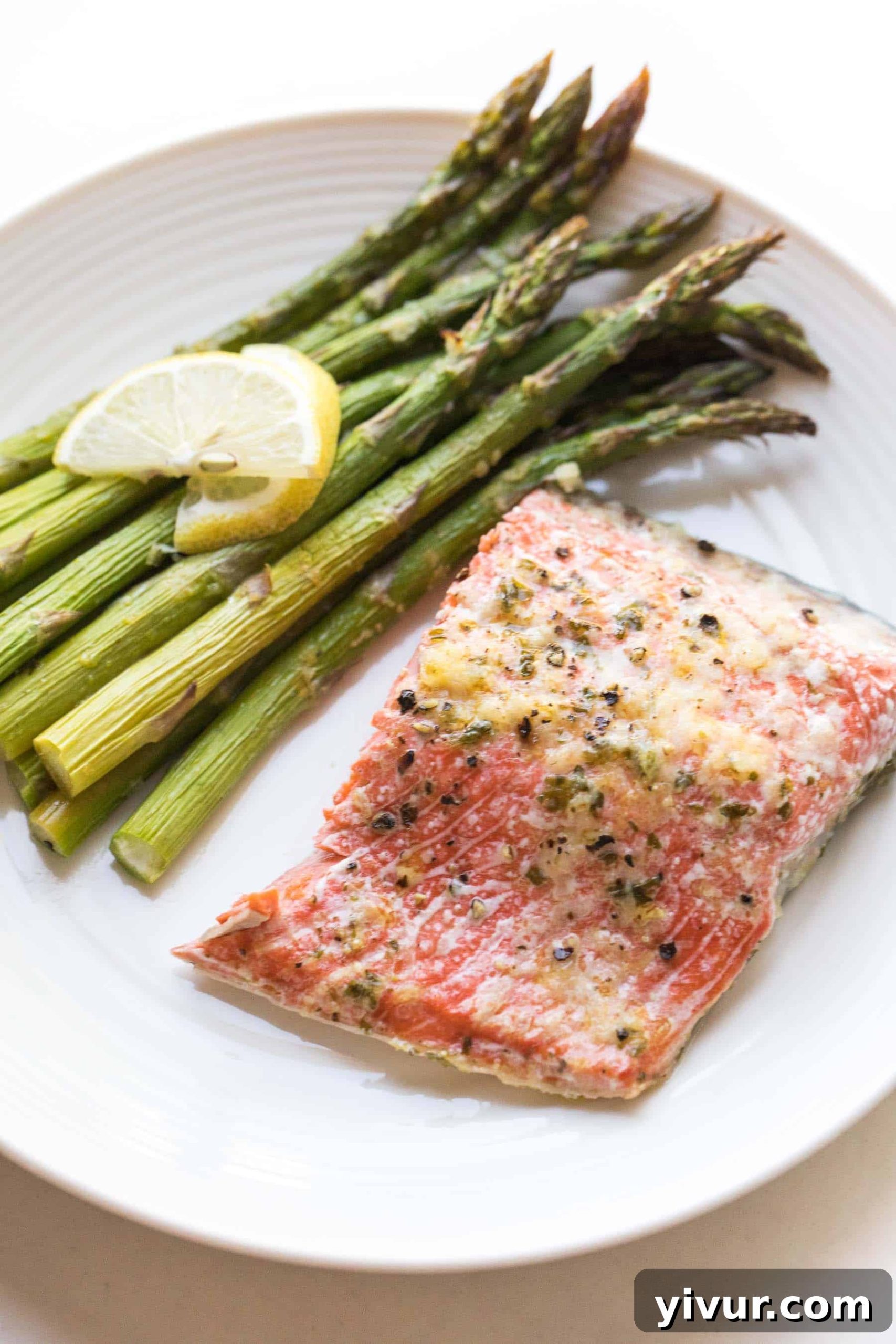 Cooked salmon and asparagus served on a white plate with lemon wedges