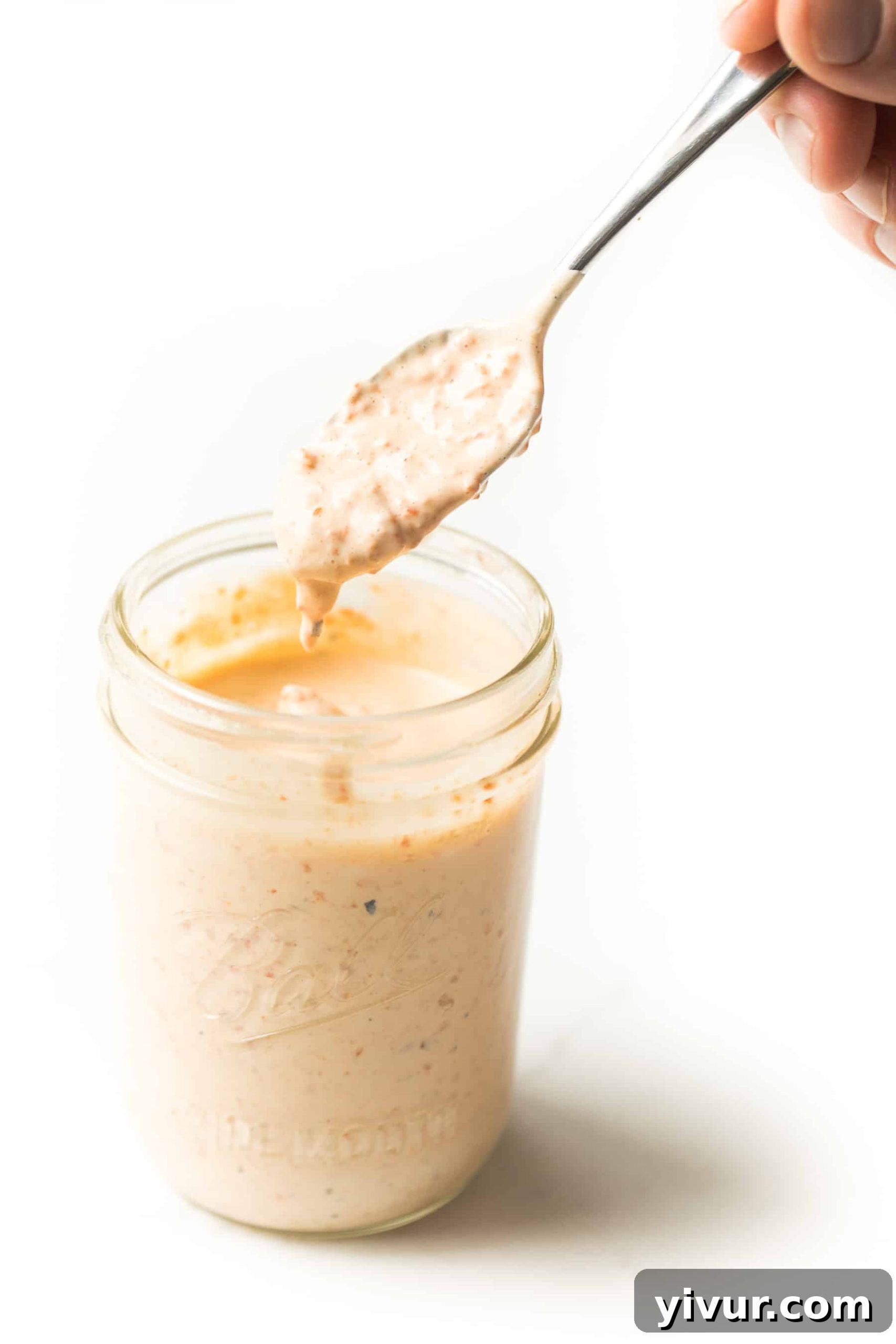 Spoon scooping out red pepper mayonnaise from a mason jar