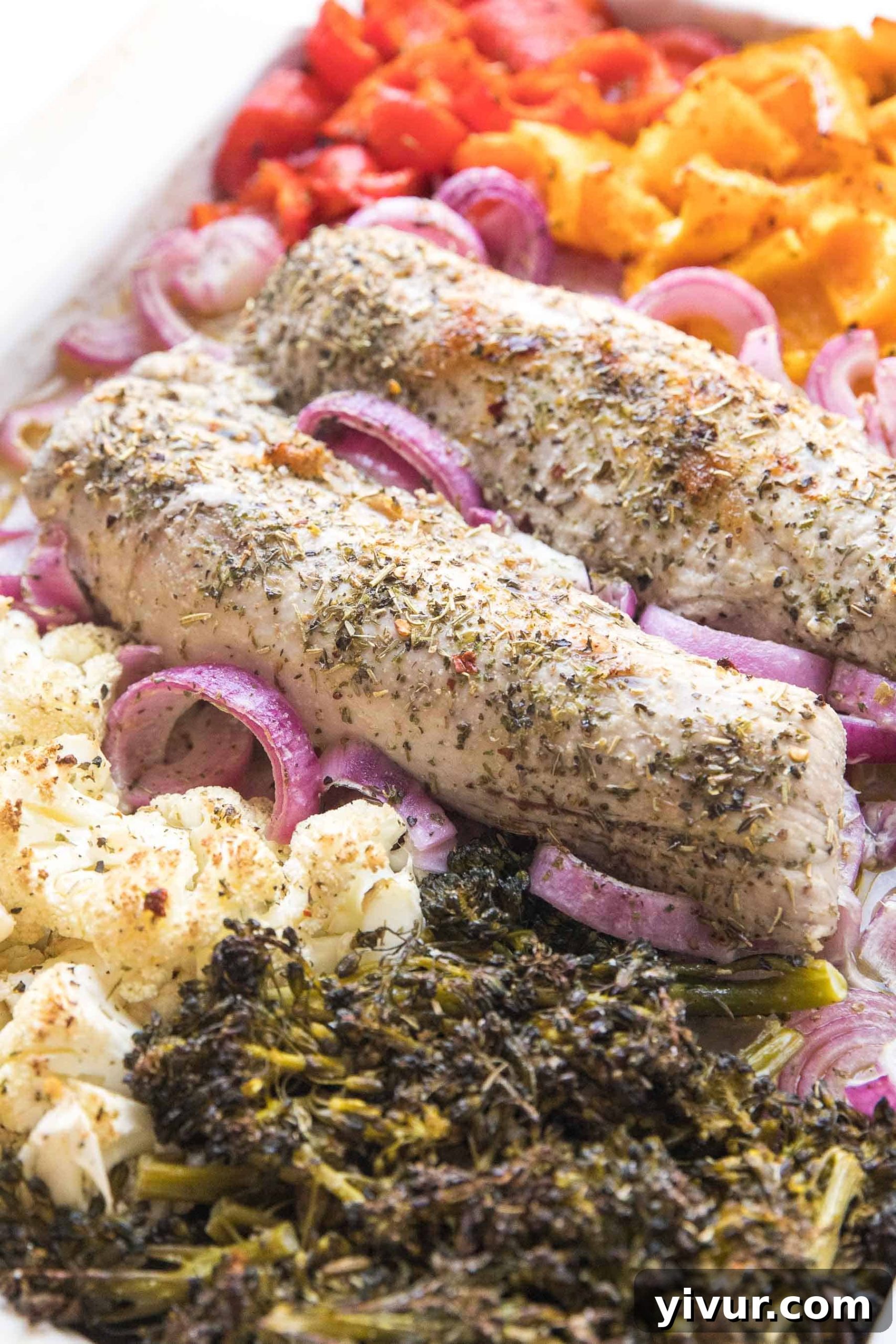 Sheet pan filled with raw pork tenderloin and colorful, chopped vegetables ready for roasting