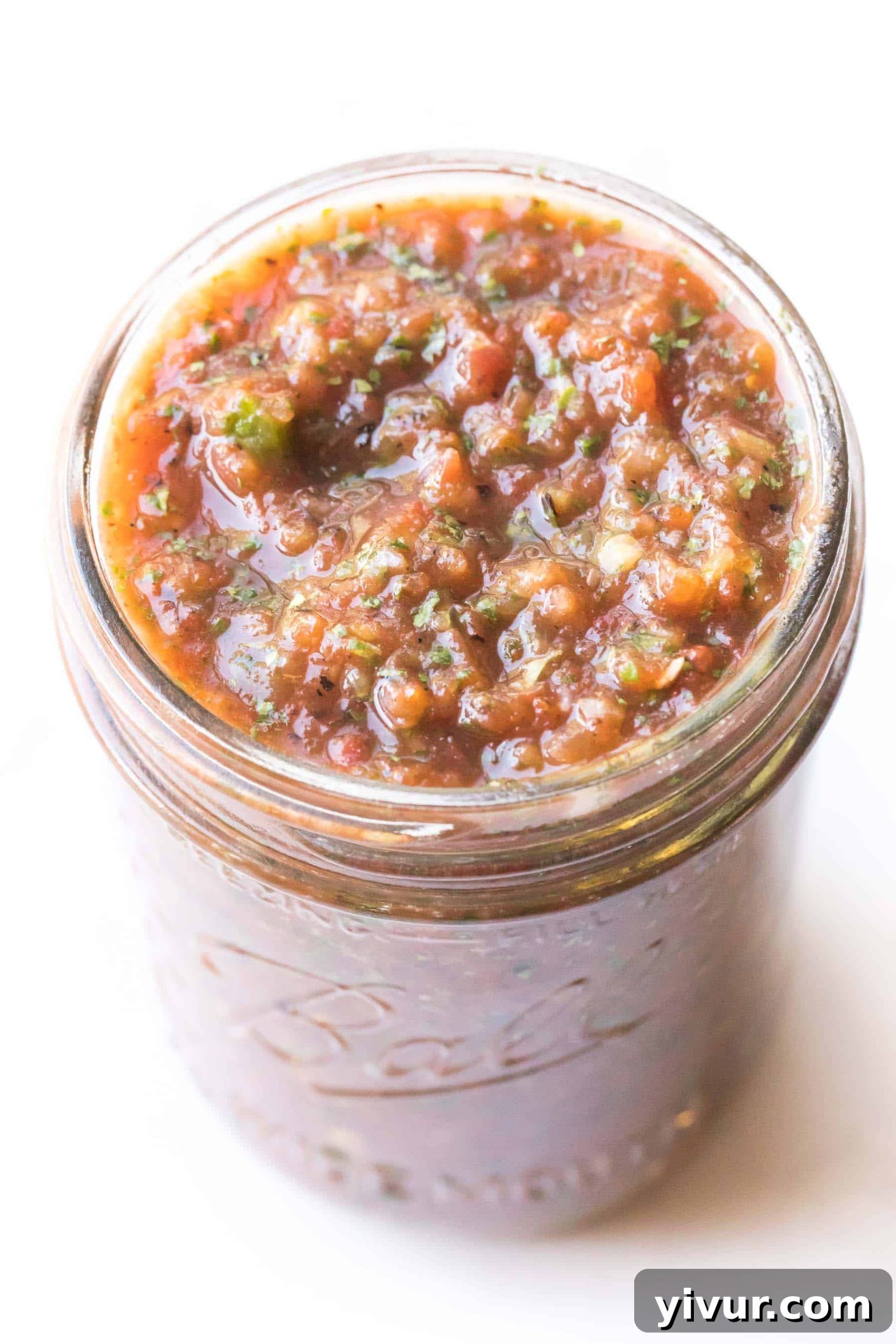 A mason jar filled with vibrant homemade red salsa, set against a clean white background, inviting a fresh culinary experience.