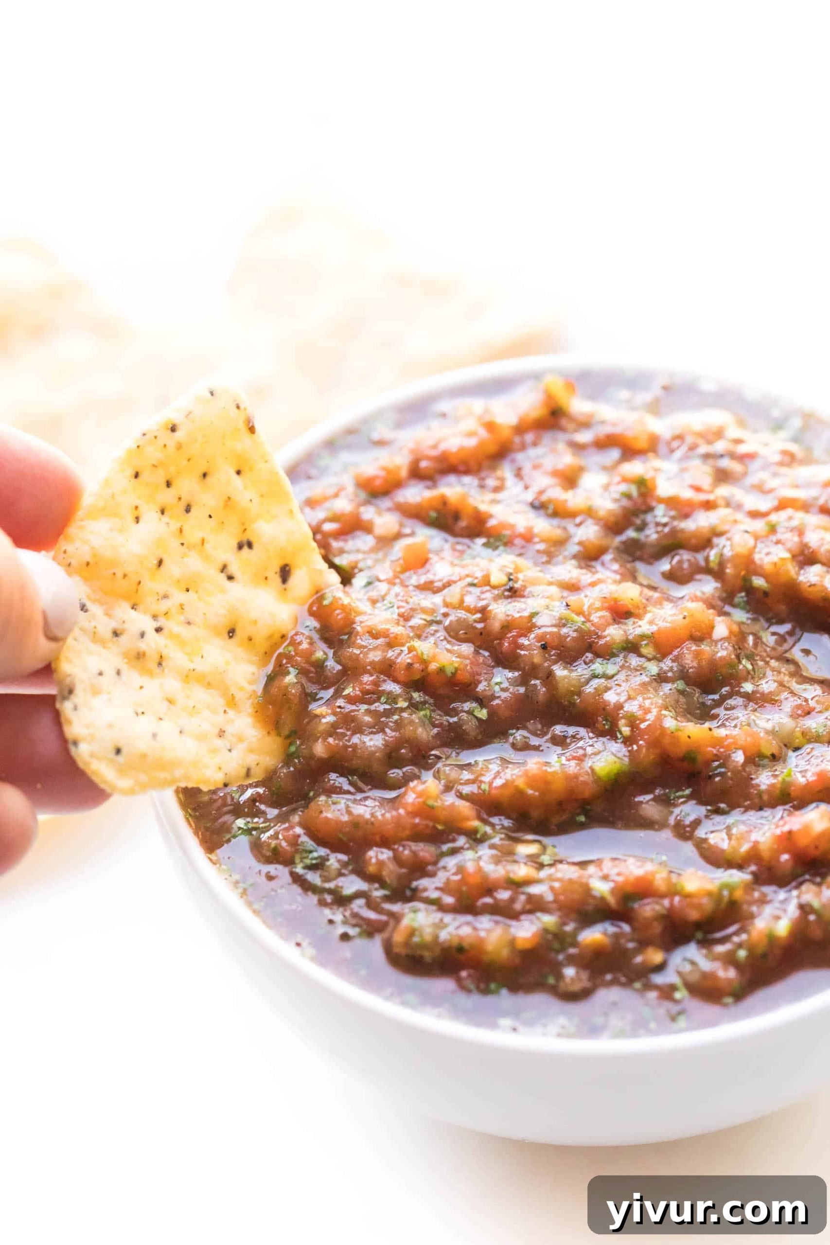A hand dipping a crispy tortilla chip into a bowl of freshly made red salsa, highlighting its perfect dipping consistency and inviting texture.