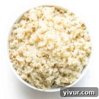 A white bowl filled with fluffy, perfectly cooked cauliflower rice on a clean white background.
