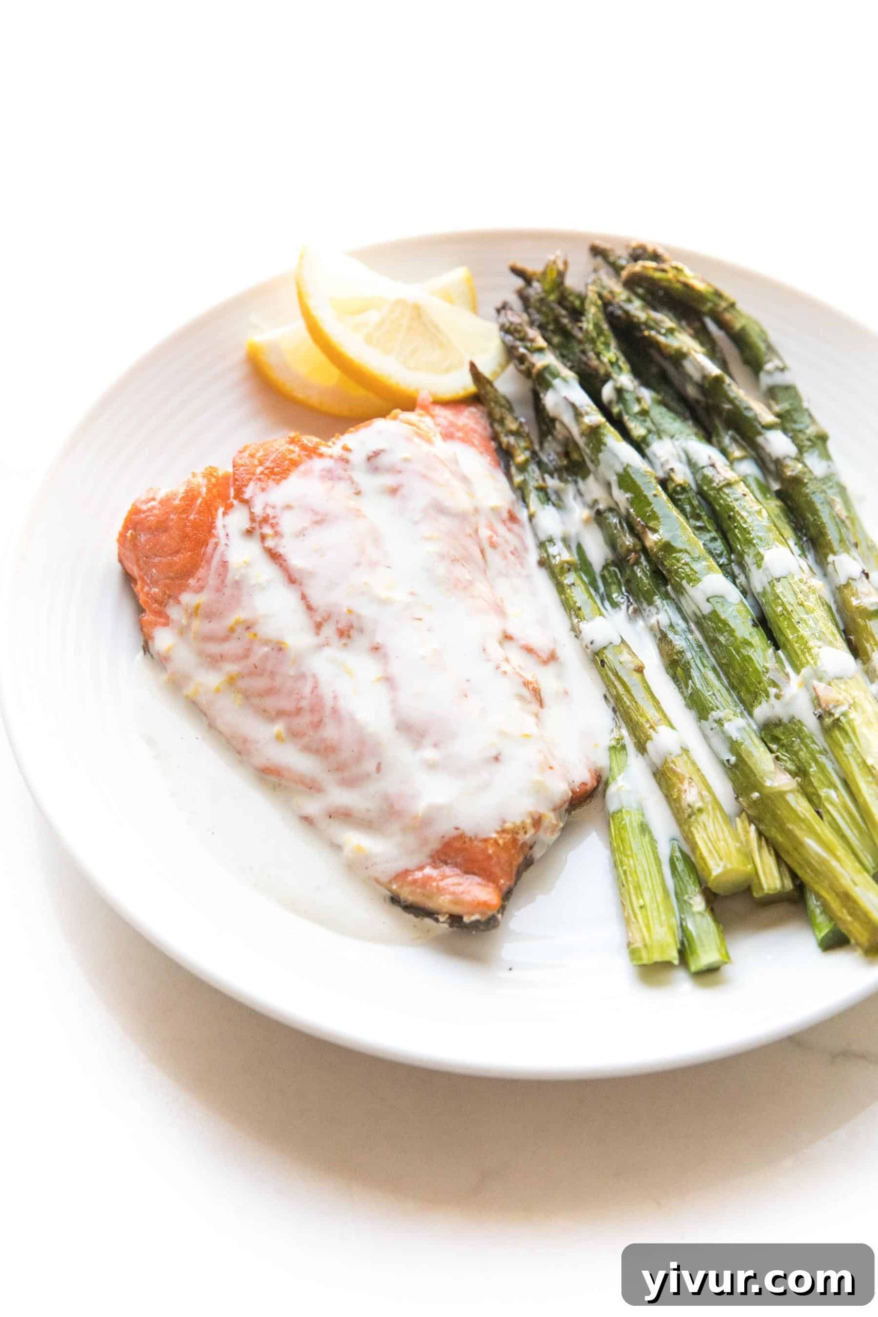 Salmon + asparagus with a white creamy coconut tahini sauce on a white plate and background