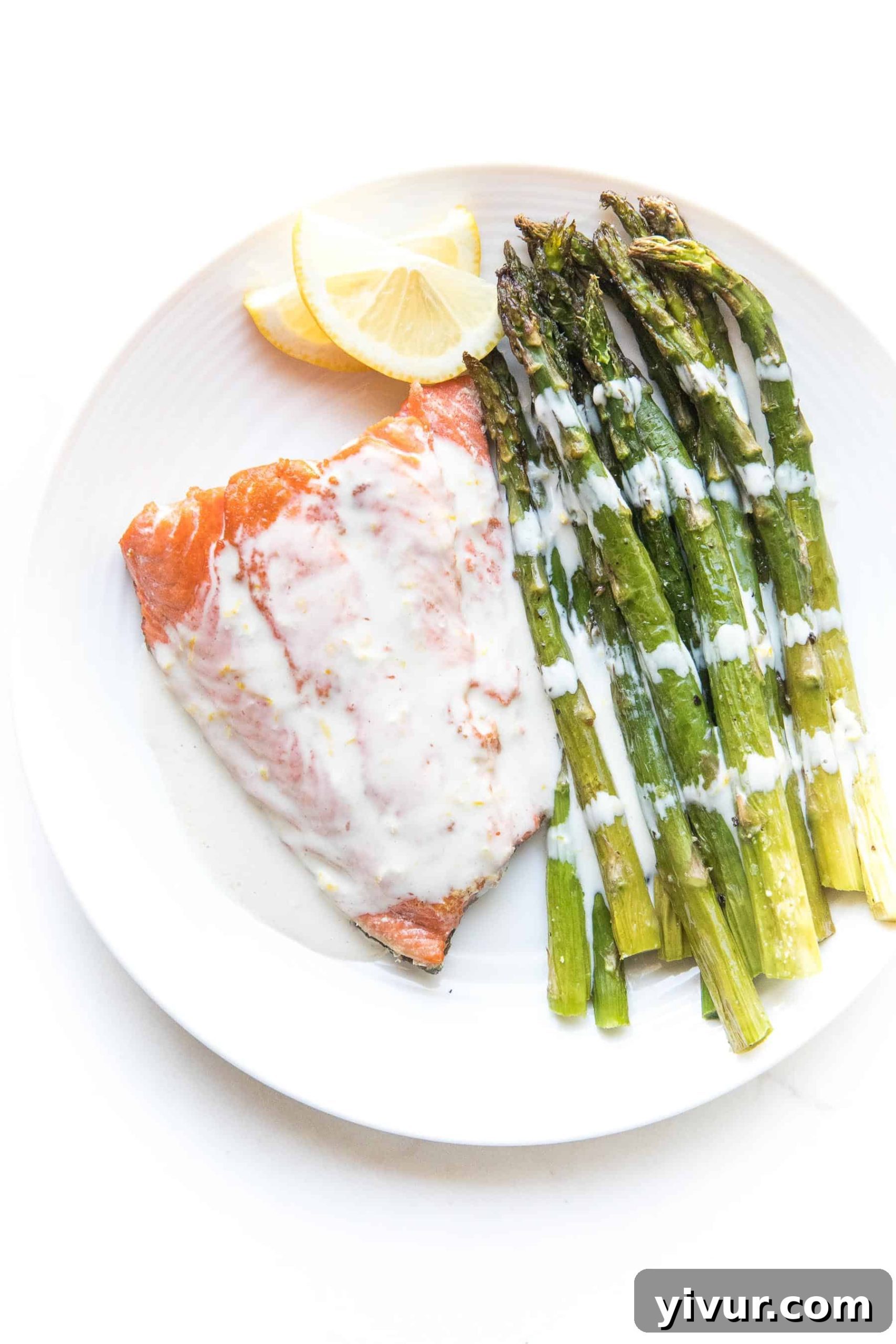 Salmon + asparagus with a white creamy coconut tahini sauce on a white plate and background