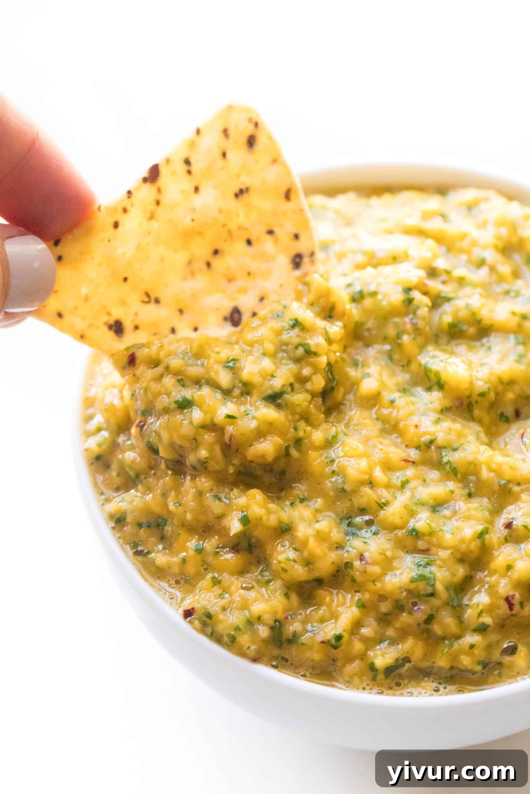 A hand dipping a tortilla chip into a bowl of fresh mango salsa on a bright white background.