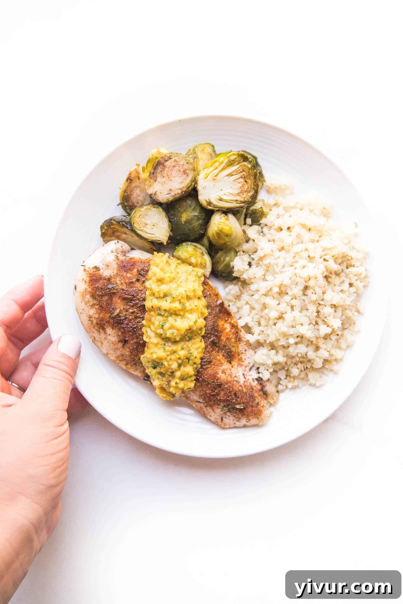 Jamaican Jerk Whole30 Keto Sheet Pan Chicken 5 hand holding a plate with jamaican chicken topped with mango salsa with brussles sprouts and cauliflower rice on a white plate