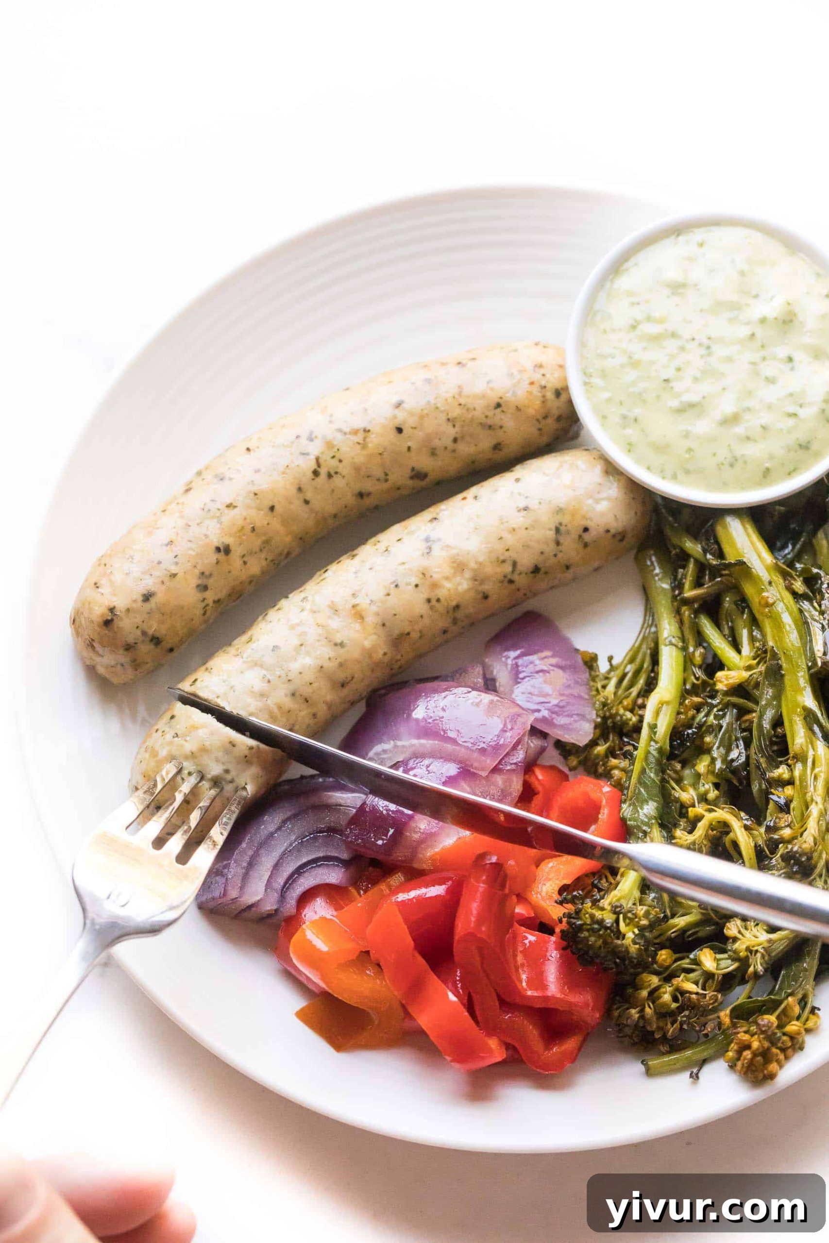 knife cutting sausages and vegetables on a white plate on a white background
