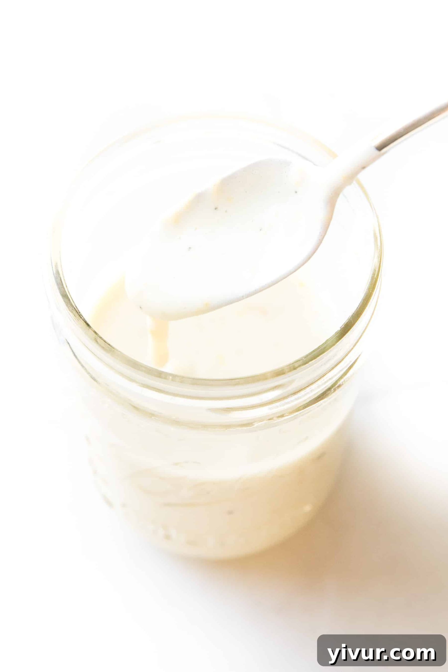 spoon pouring a white lemon garlic aioli sauce into a white mason jar on a white background