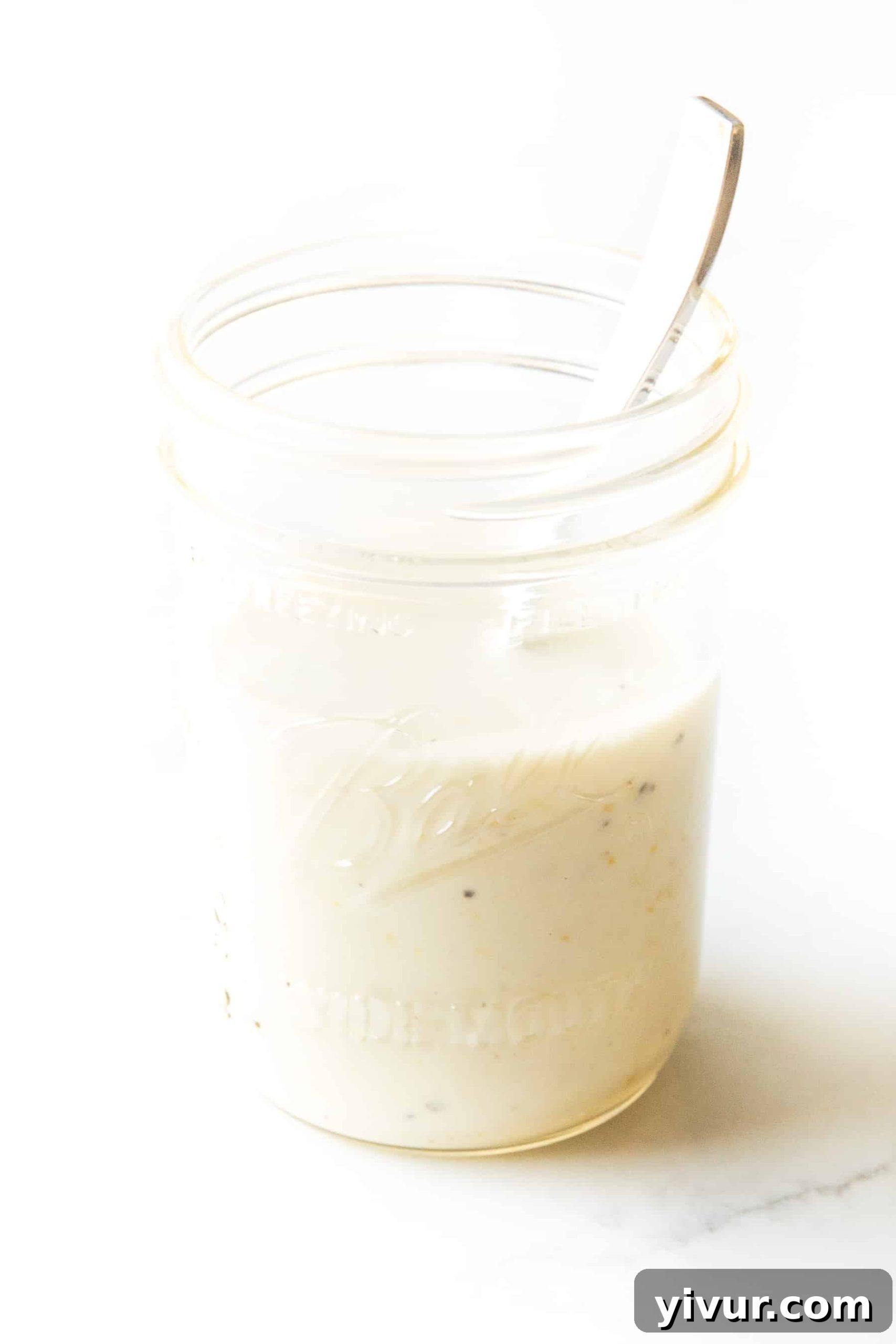 white lemon garlic aioli sauce in a mason jar with a spoon inside on a white background