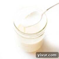 spoon pouring a white sauce into a mason jar on a white background
