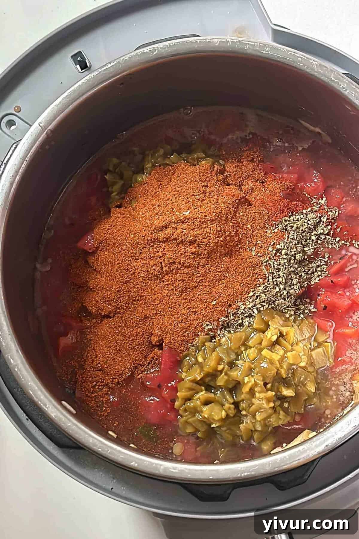 Keto Whole30 Instant Pot Chili Beanless and Easy 6 A top-down view of chili spices, including chili powder, cumin, oregano, and smoked paprika, generously sprinkled over browned ground beef and sautéed vegetables in an Instant Pot, just before being stirred in.