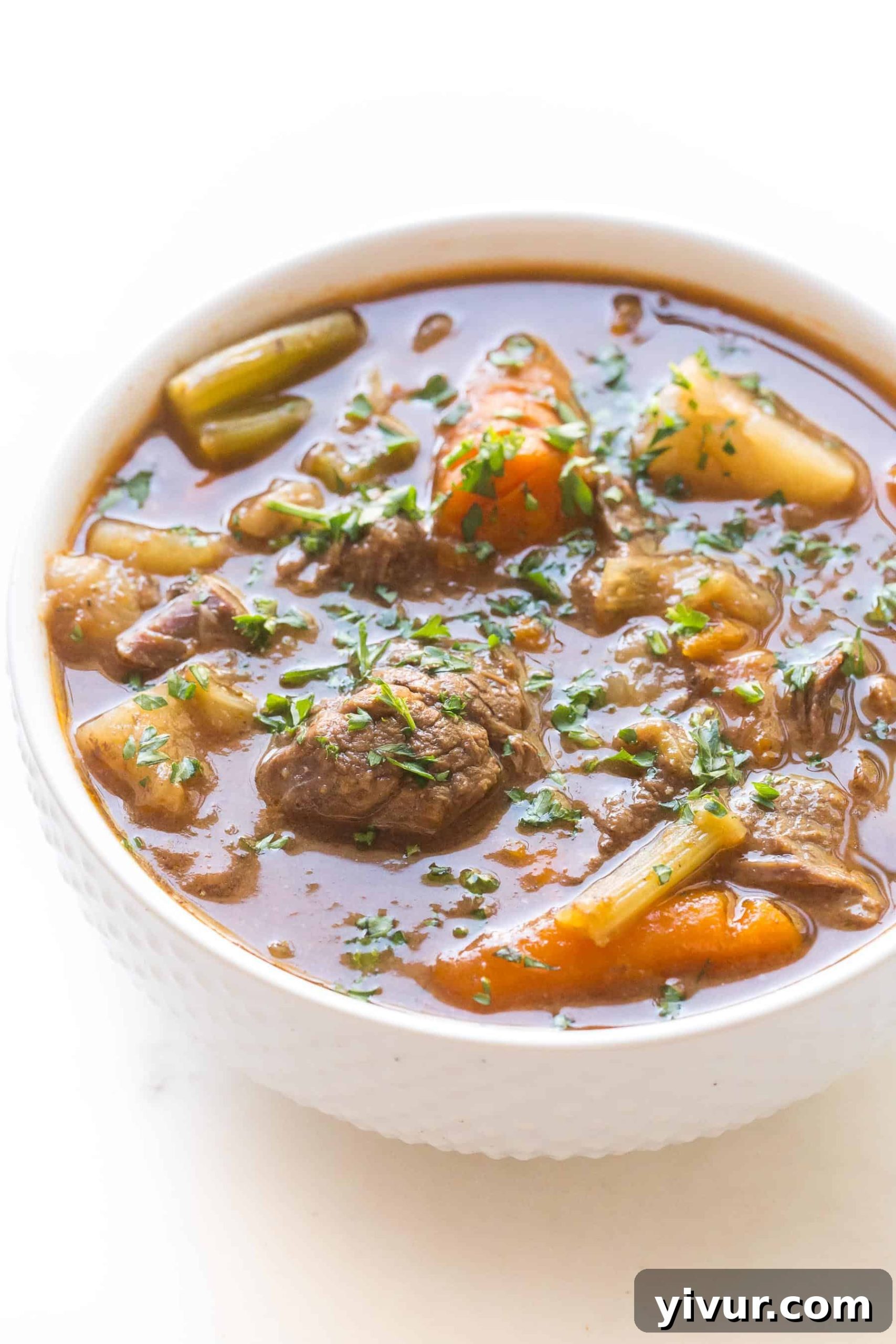 A steaming bowl of Whole30 Keto Instant Pot Beef Stew, rich with tender beef chunks and colorful vegetables, served in a white bowl on a light background, garnished with fresh herbs.