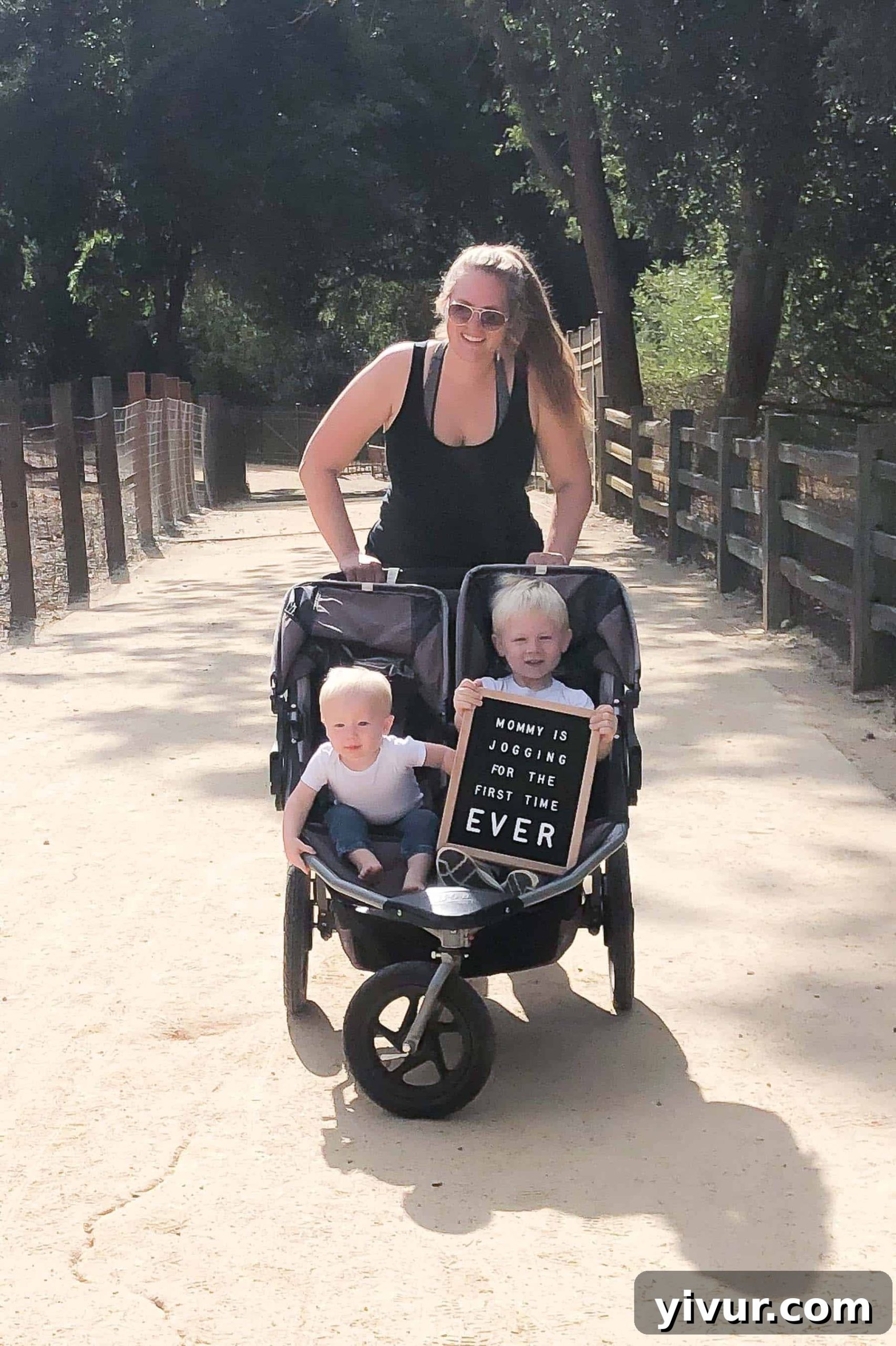 Mom pushing her 2 boys in a double stroller with a letterboard message saying Mommy is jogging for the first time ever