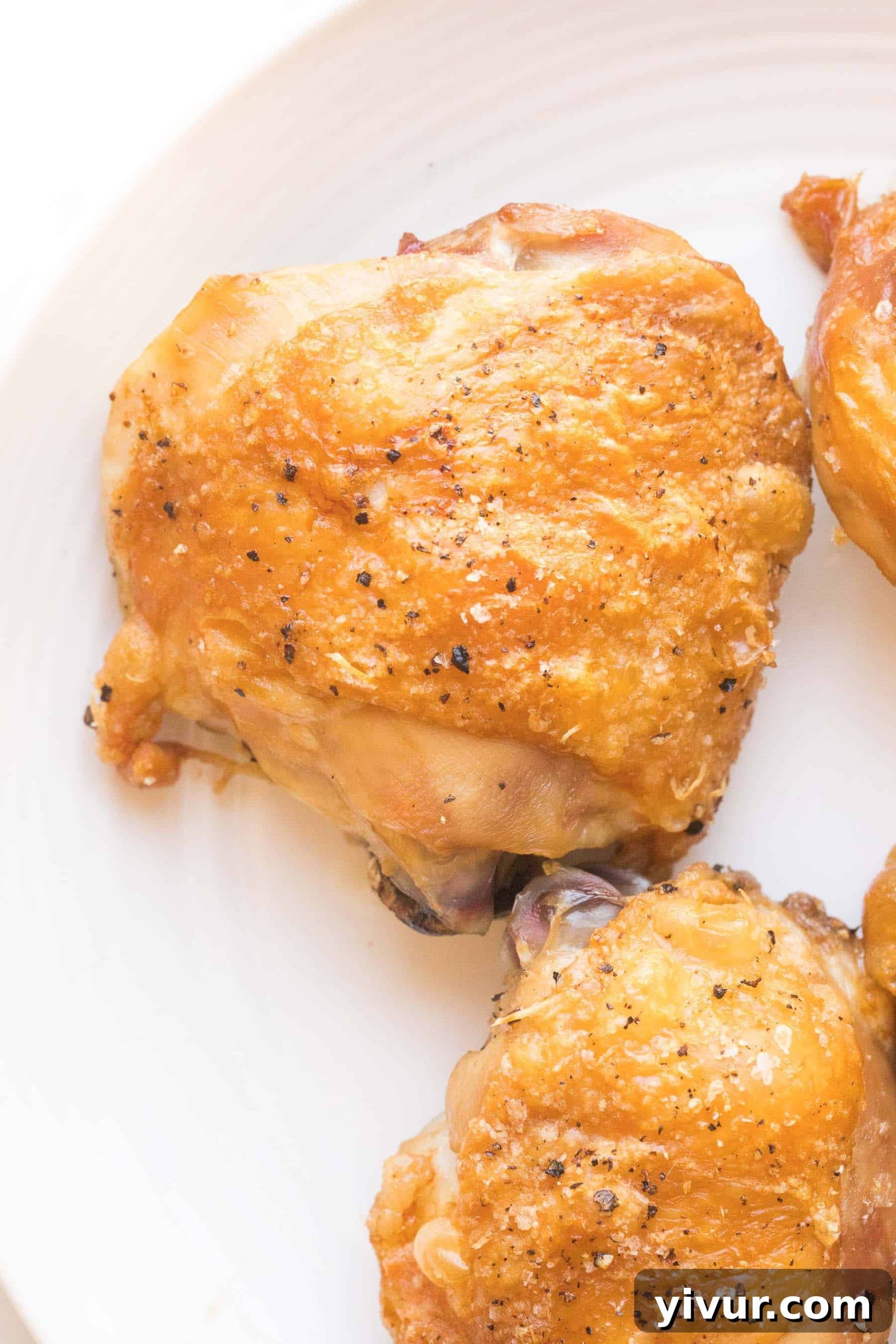Close up of a crispy golden brown chicken thigh on a white plate, showcasing its perfectly rendered skin