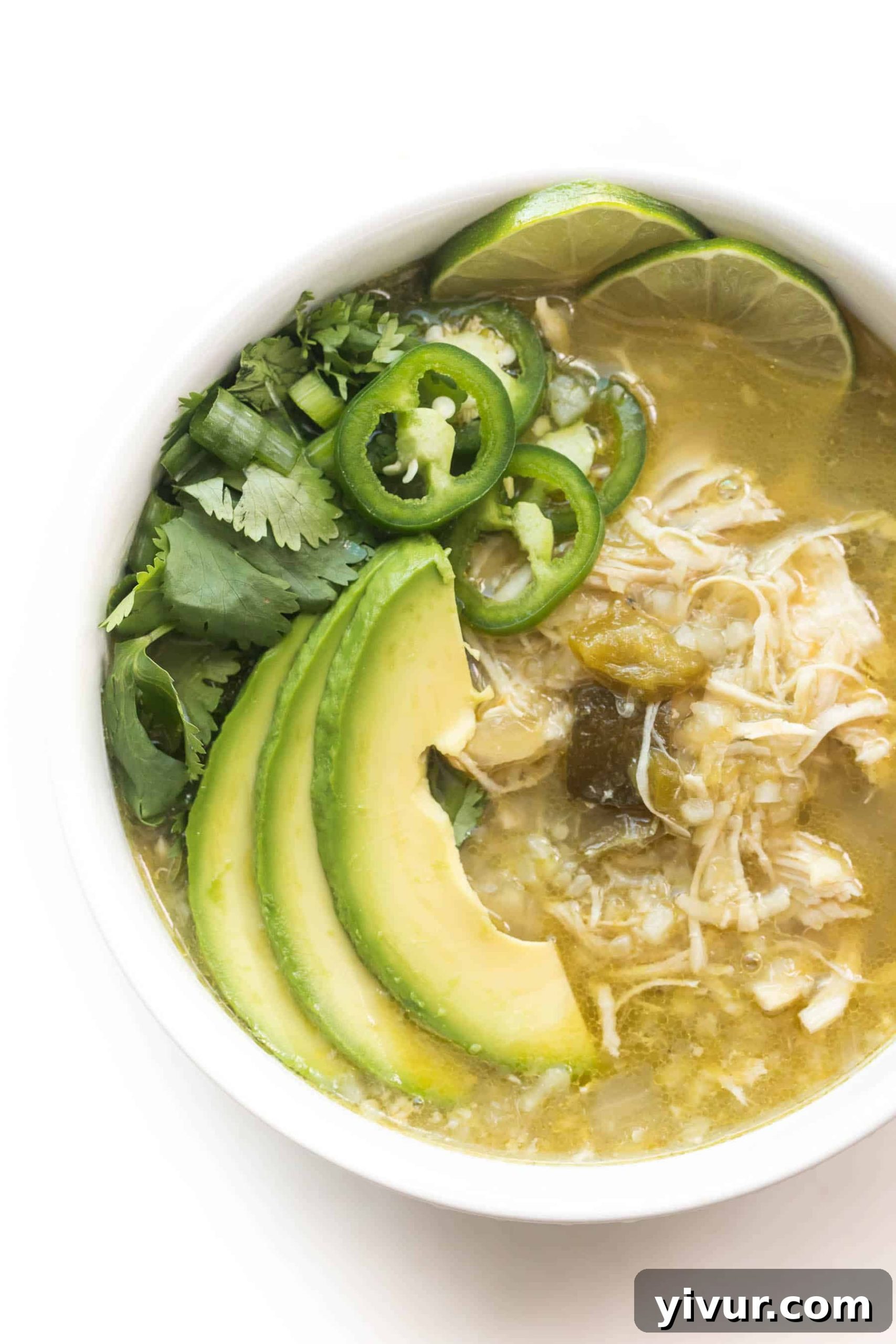 Effortless Whole30 Keto Instant Pot Verde Chicken Chili 2 A bowl of vibrant green Verde Chicken Chili, garnished with fresh cilantro and lime wedges, sitting on a crisp white background. This hearty, low-carb dish is perfect for Whole30 and Keto diets, boasting a rich blend of flavors and healthy ingredients.