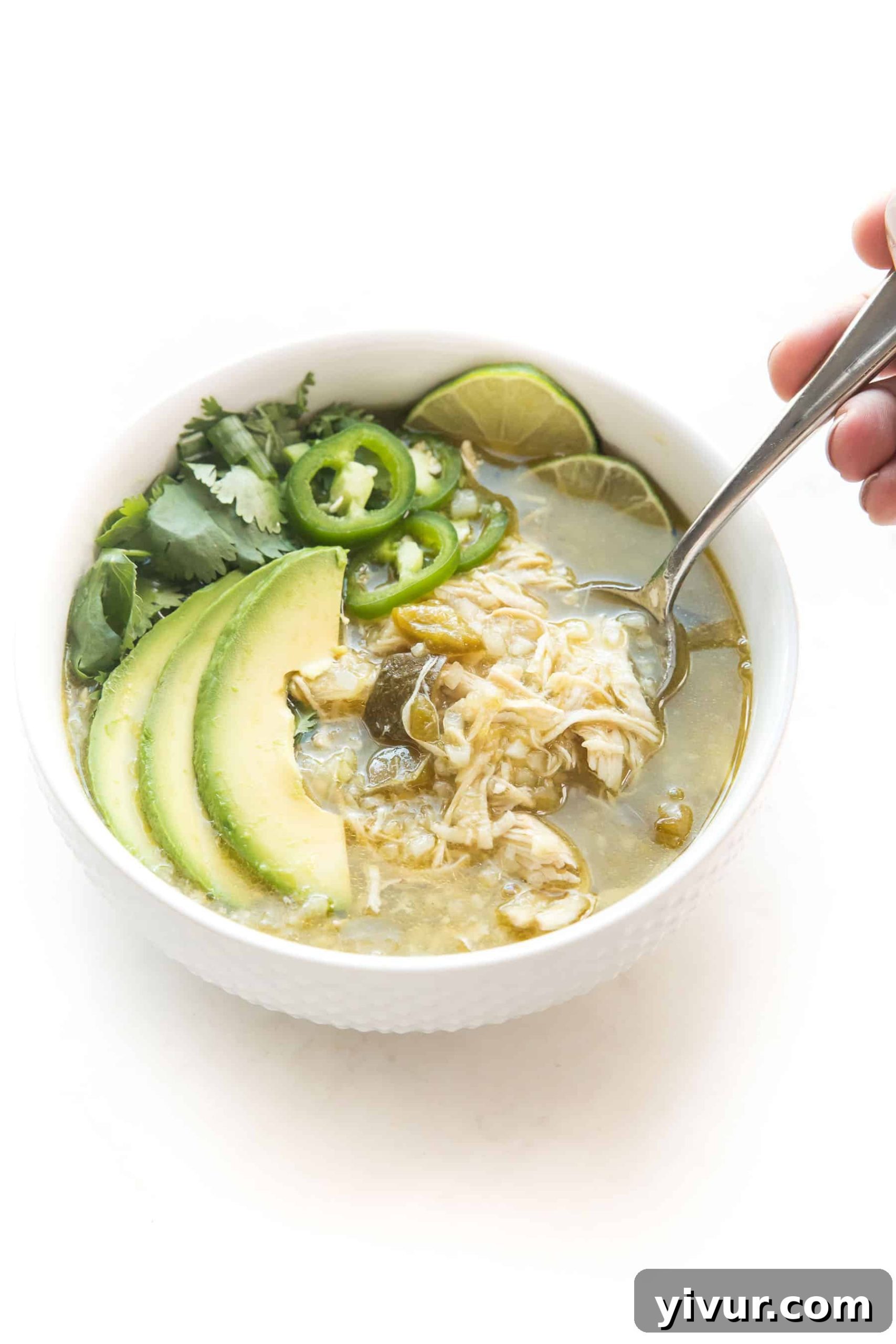 Effortless Whole30 Keto Instant Pot Verde Chicken Chili 3 A close-up shot of a spoon scooping into a bowl of green Verde Chicken Chili, highlighting the rich texture of the chicken and vegetables. The chili is garnished with fresh toppings, ready to be enjoyed as a wholesome, low-carb meal.