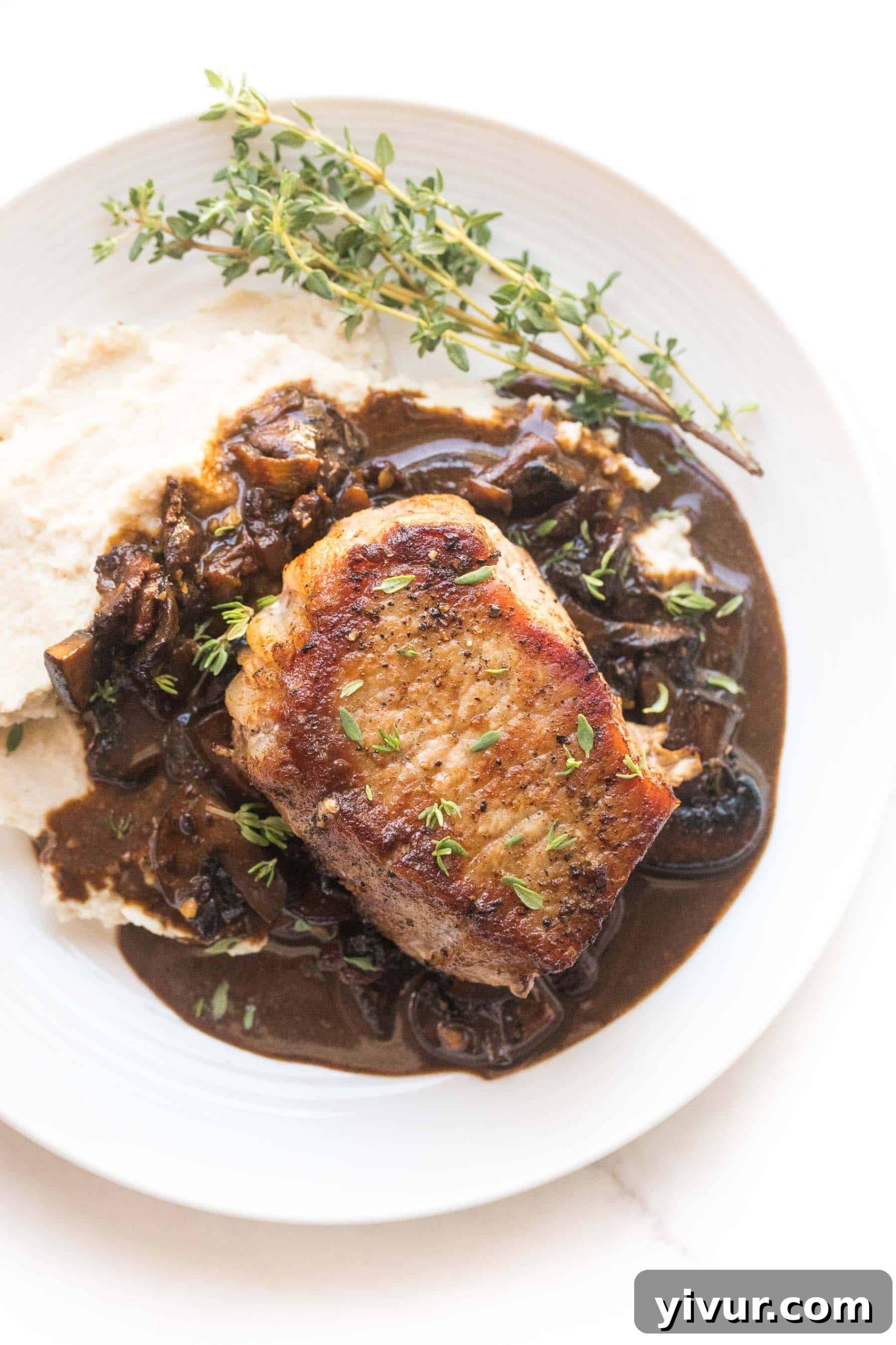 Ultimate Whole30 Keto Pork Chops with Creamy Bacon Mushroom Sauce 2 Succulent Whole30 Keto Pork Chops with rich Bacon Mushroom Sauce served alongside creamy mashed cauliflower, garnished with fresh thyme.