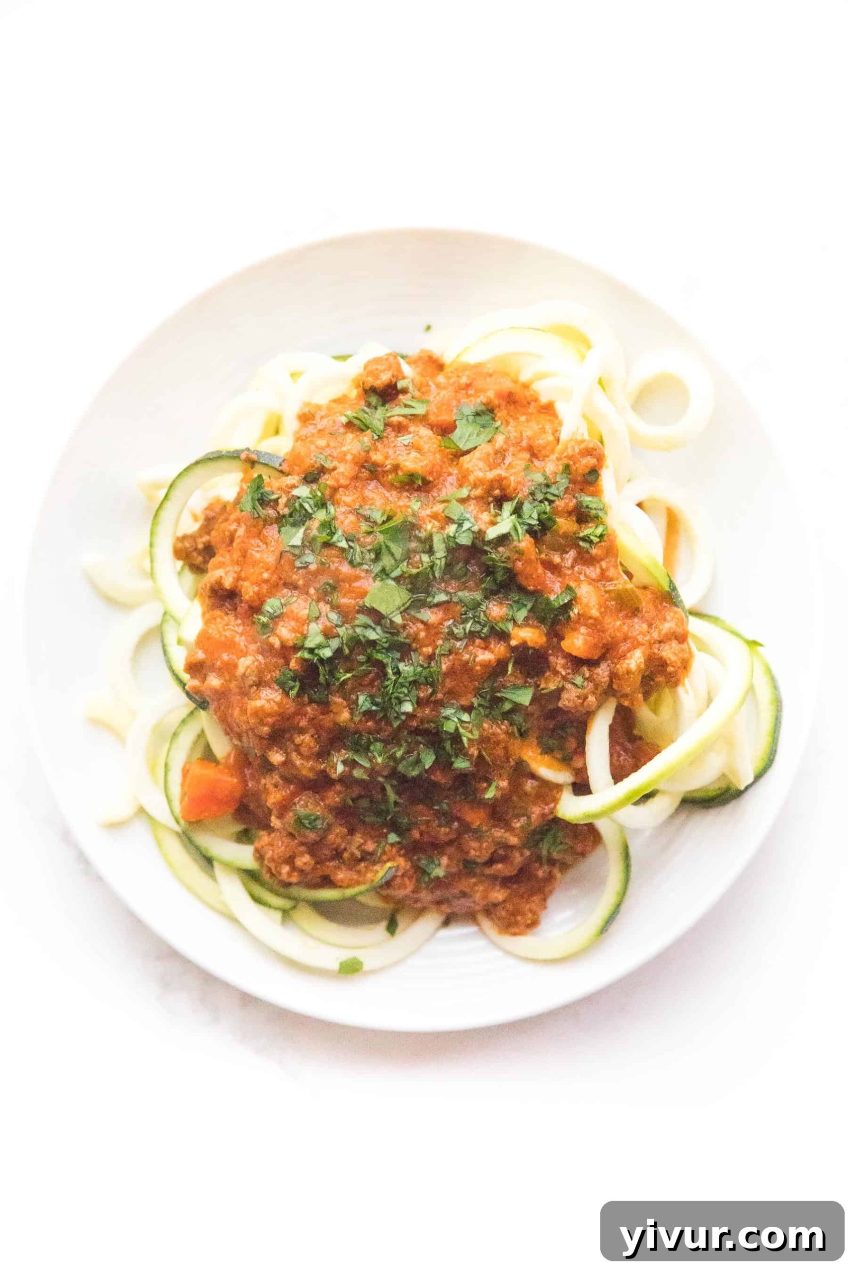 Zucchini noodles with red bolognese sauce on a white plate and background